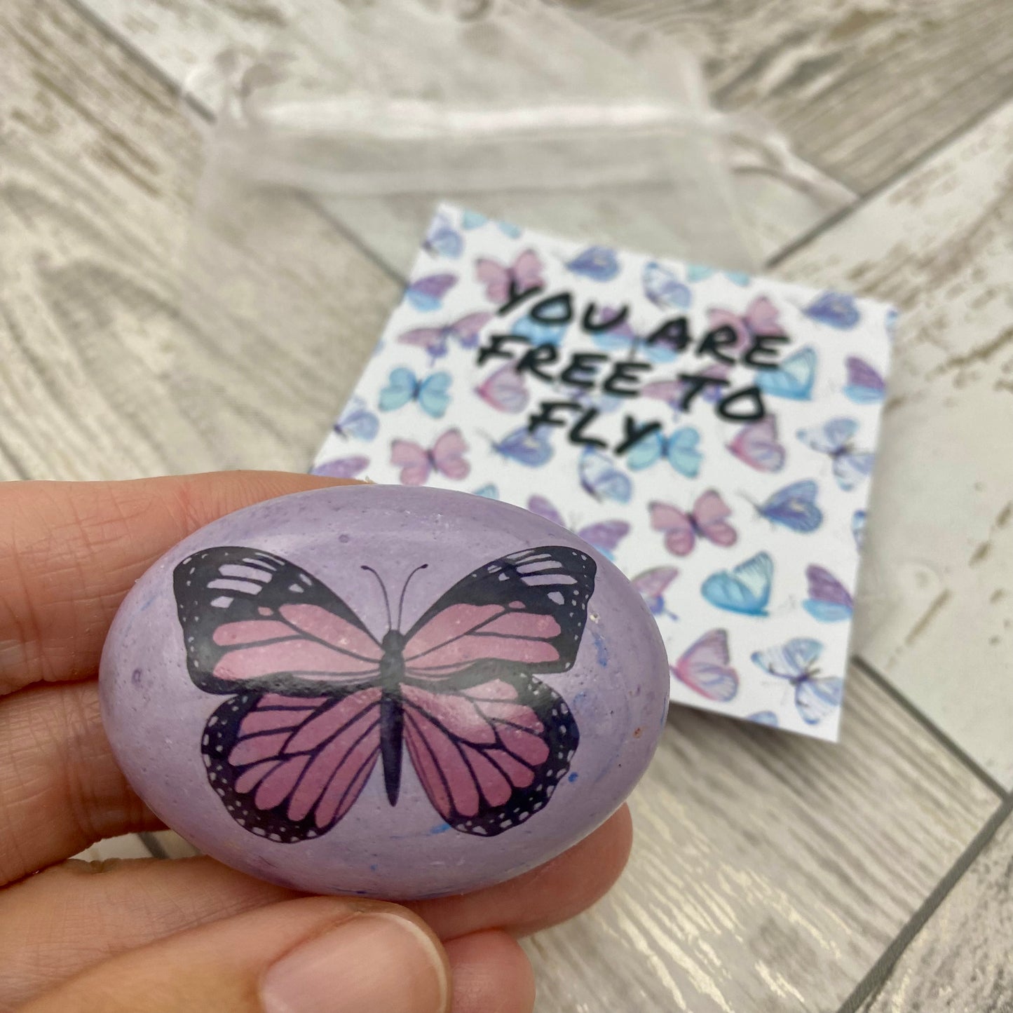 Pink butterfly decal on a marbled pebble with an affirmation card reading "You are free to fly"