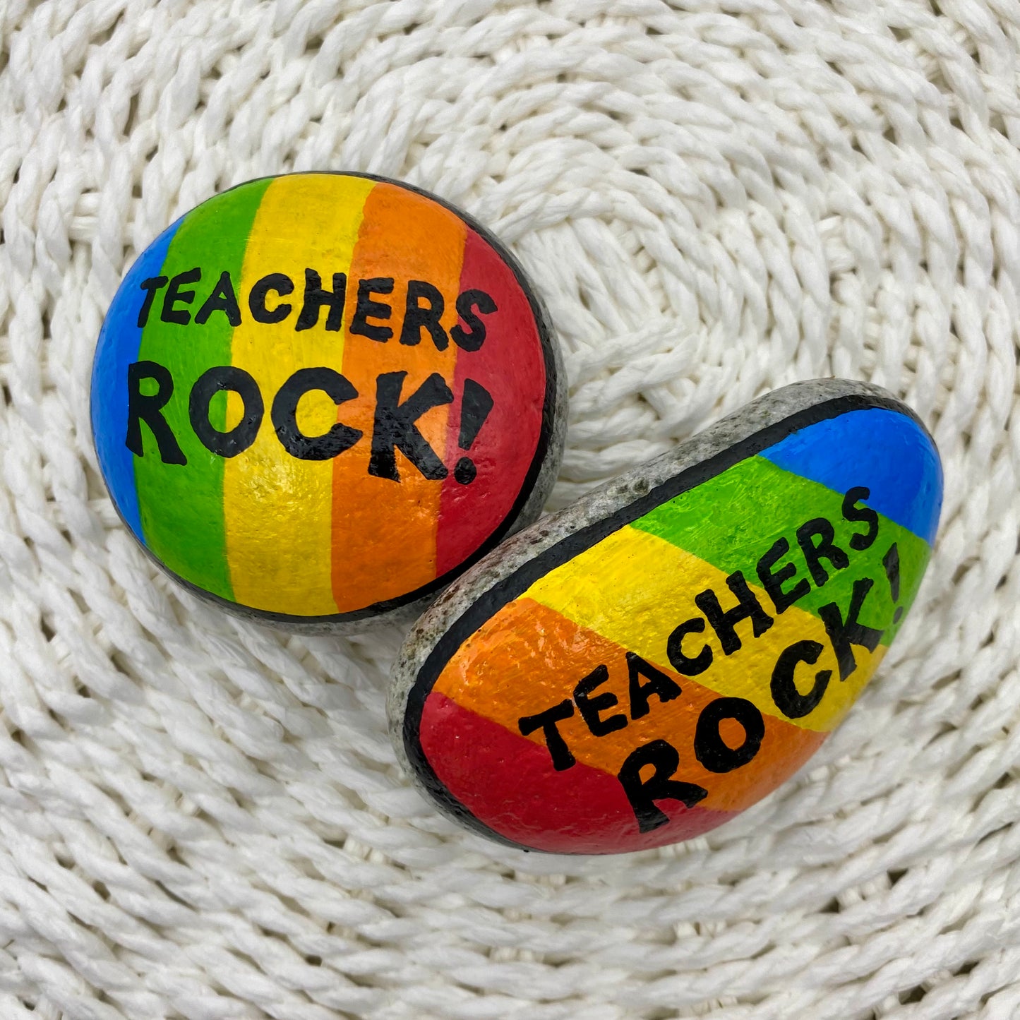 2 rocks painted with bright rainbow stripes and the words"Teachers Rock" written on.