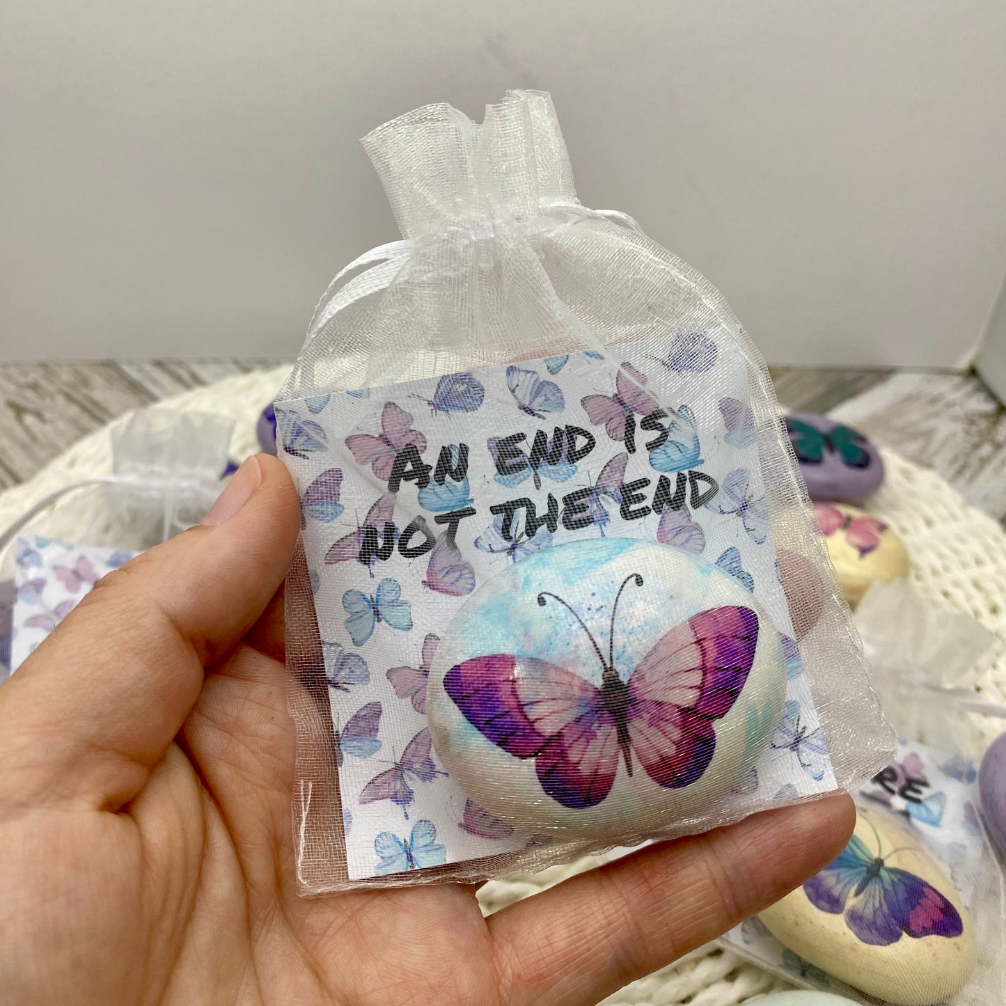 Pink butterfly decal on a marbled pebble with an affirmation card reading "An end is not the end" in an organza bag