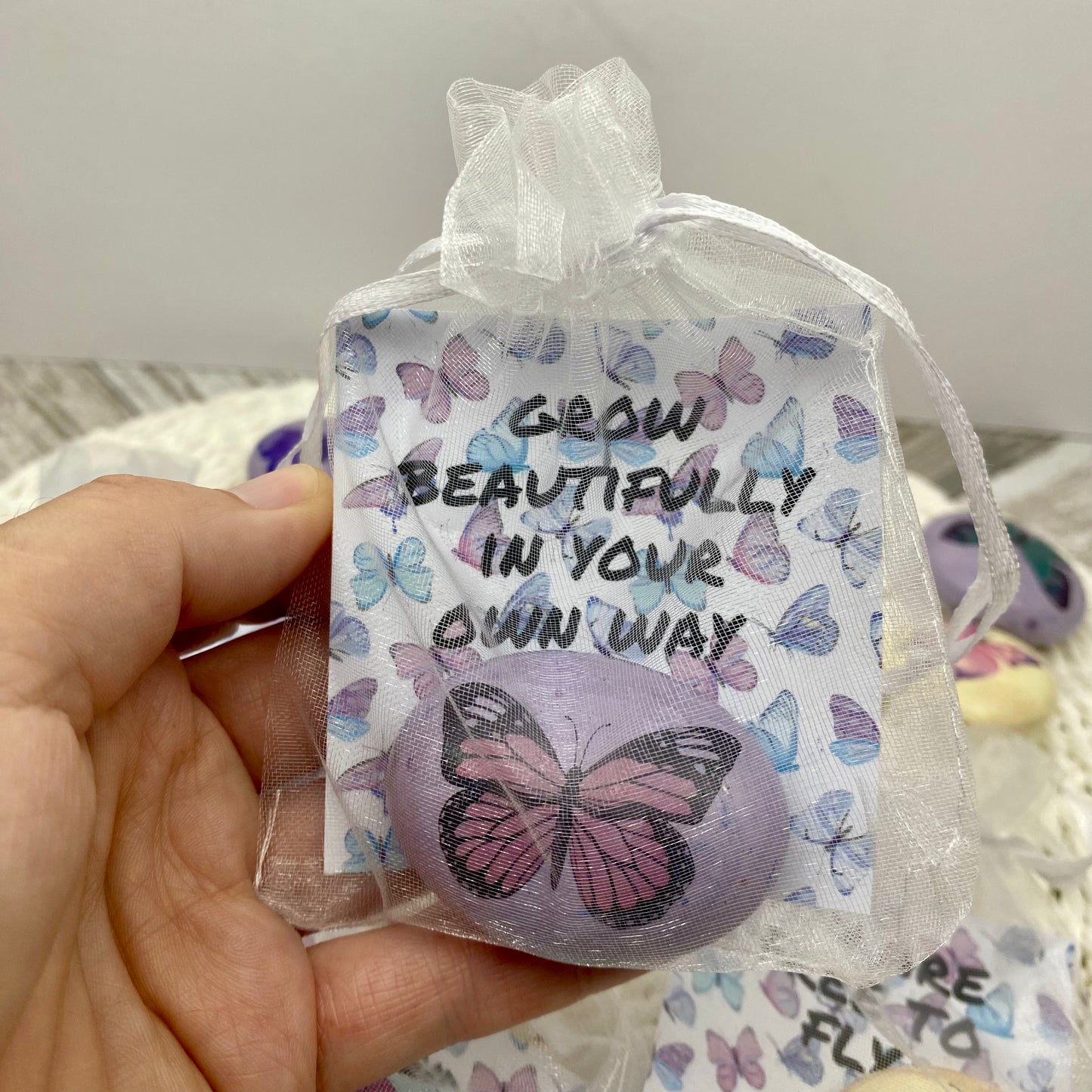 Pink butterfly decal on a marbled pebble with an affirmation card reading "Grow beautifully in your own way" in an organza bag