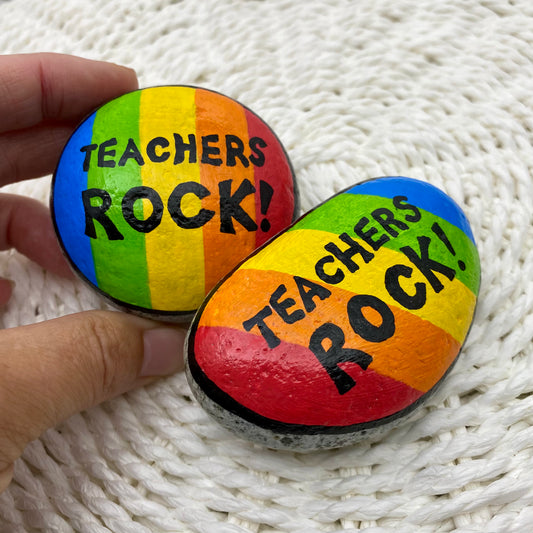 2 rocks painted with bright rainbow stripes and the words"Teachers Rock" written on.