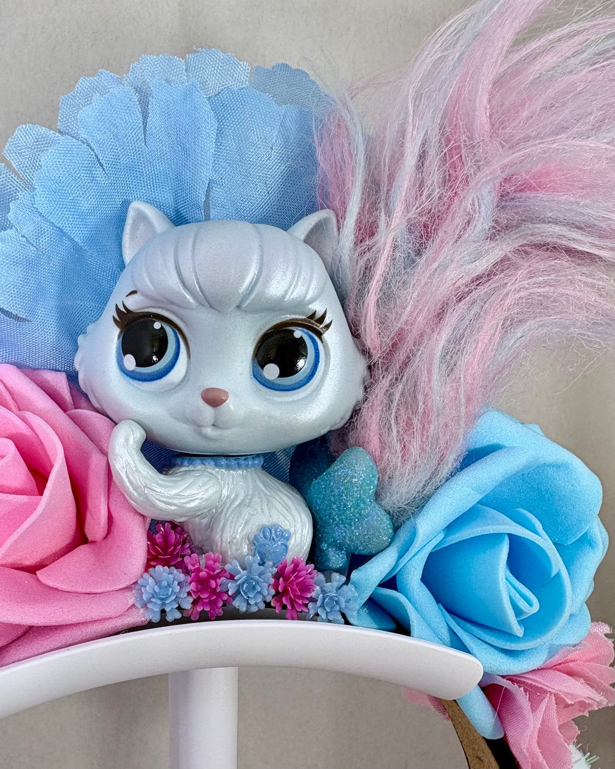 Close up of Pale Pink and Blue headband with floral design and small cat toy figure