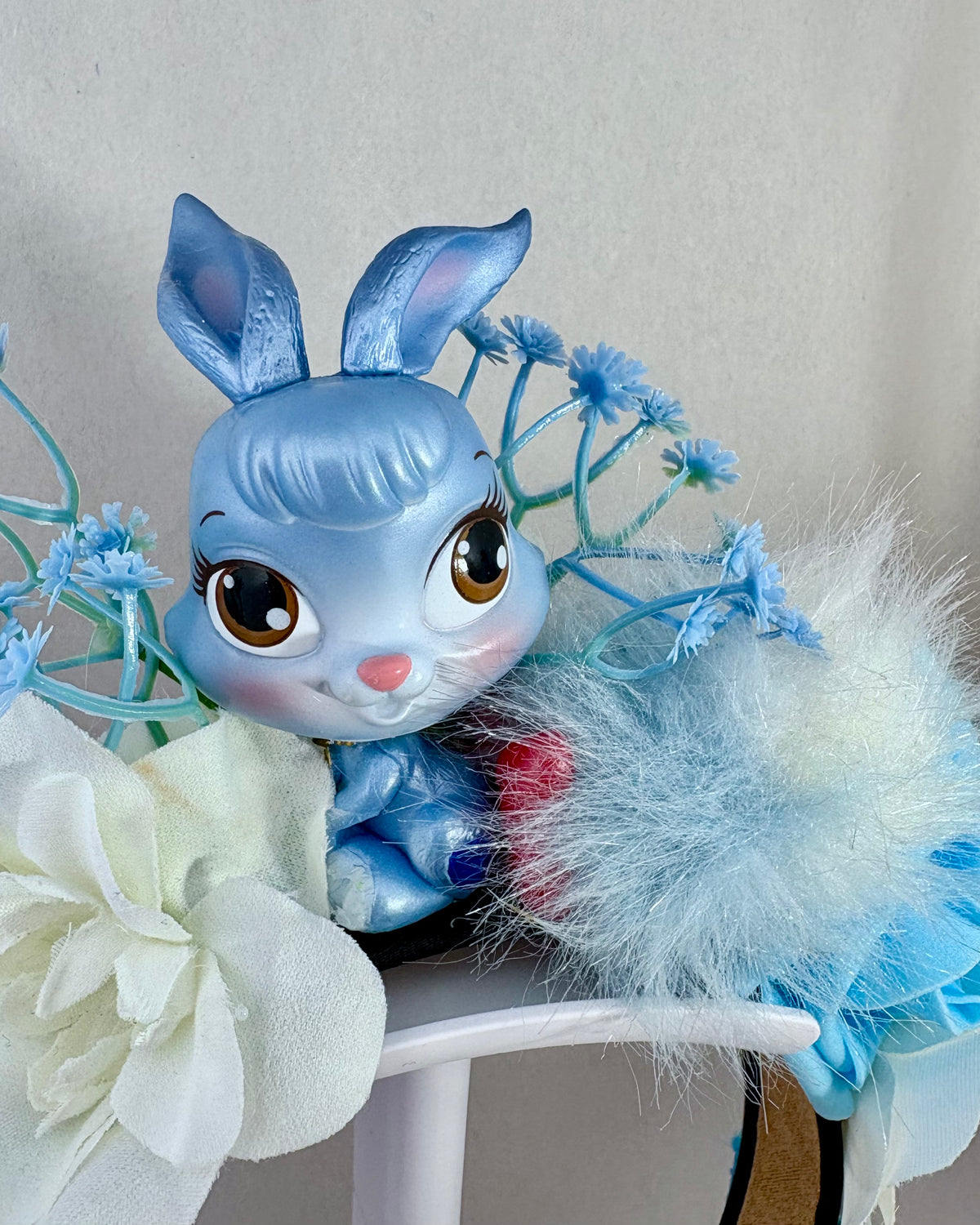 Blue rabbit toy figurine with large eyes and a fluffy tail, surrounded by flowers on a headband