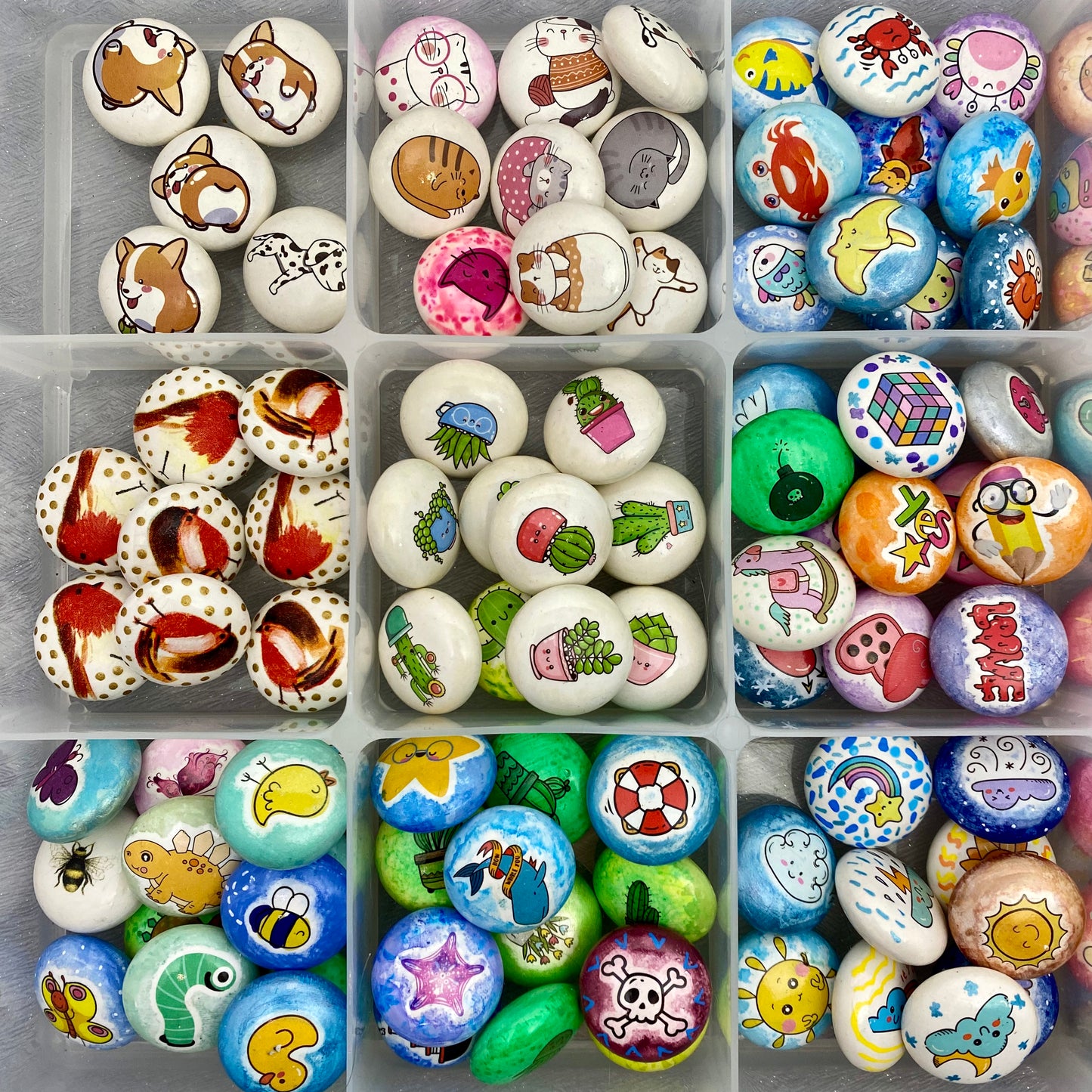 Lots of colourful mini pebbles in a tray, sorted by theme. Dogs, Cats, Birds, Insects, Plants, Ocean, Love, Toys, Weather.