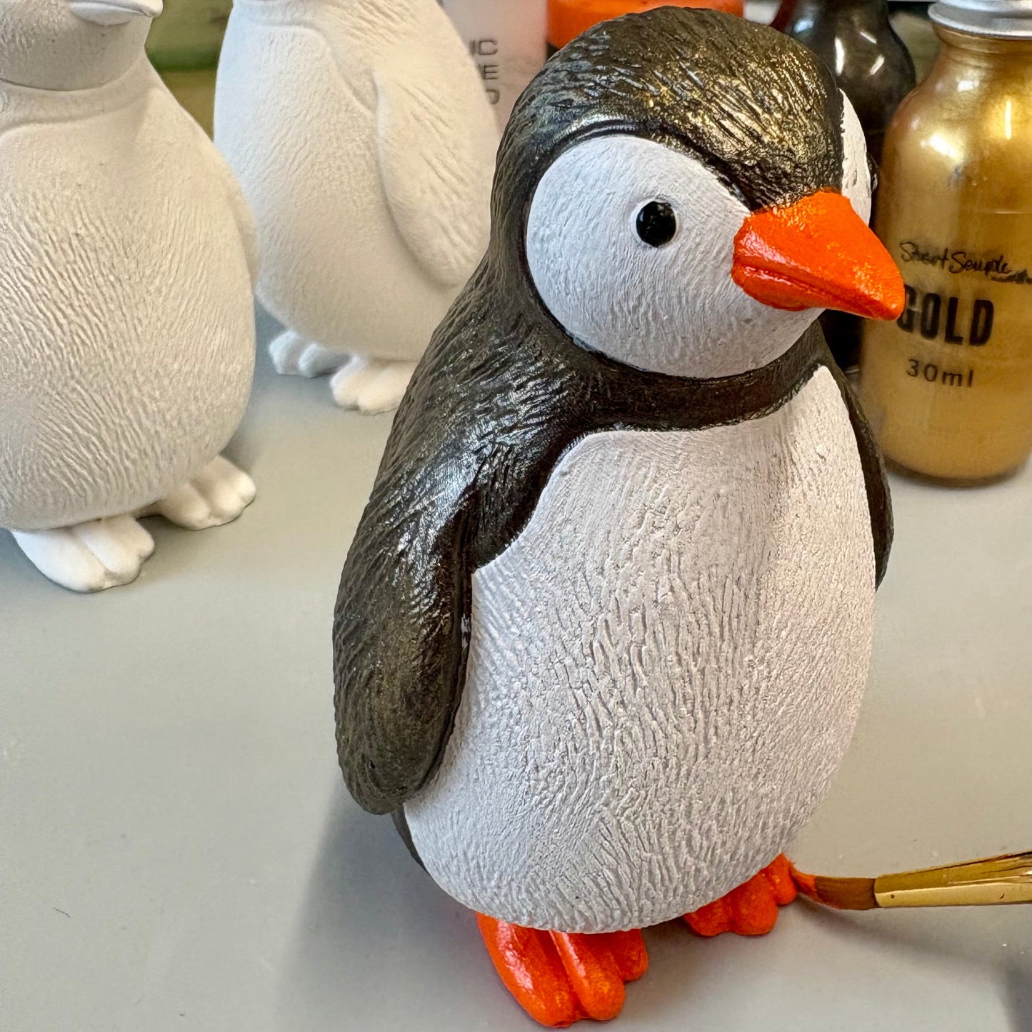 Painted penguin statue with penguin blanks and paints in the background
