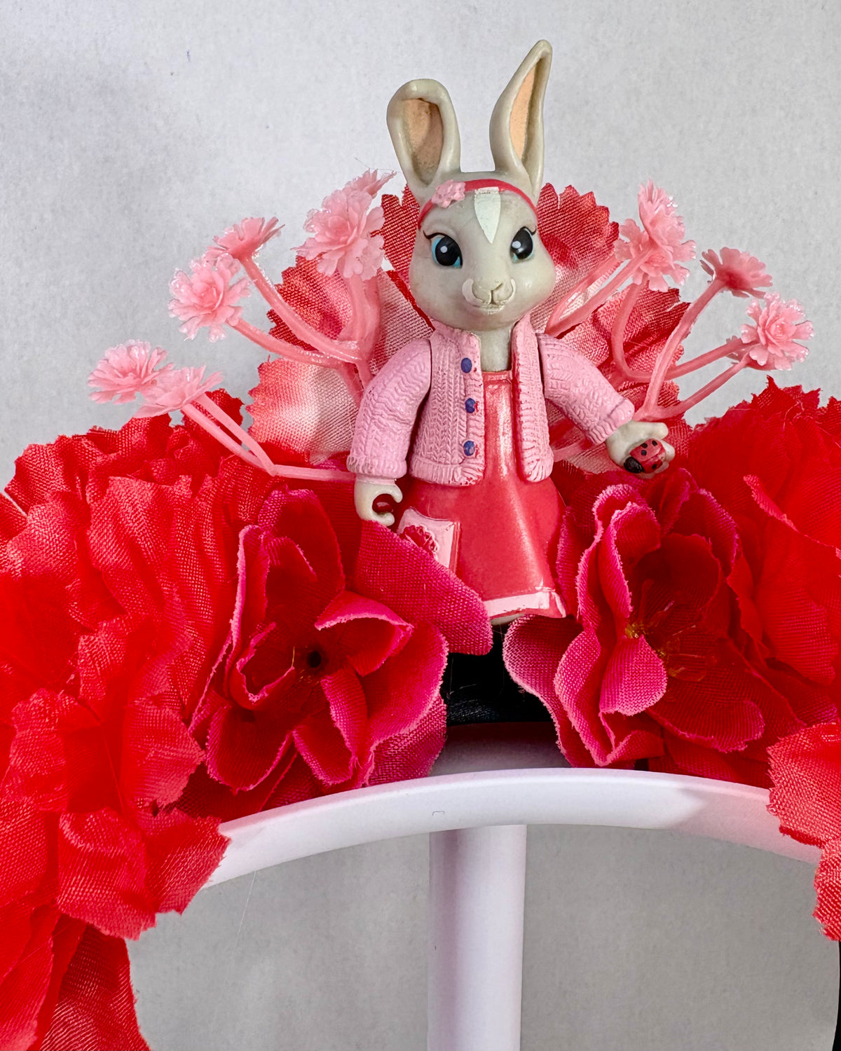 Toy rabbit in a pink outfit surrounded by red flowers on a festival crown headband
