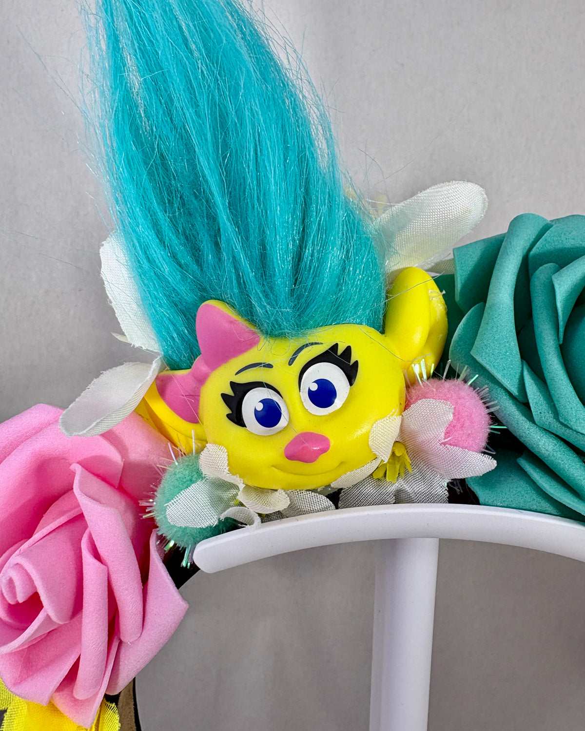 Close up of Colourful Festival Crown with pink, yellow and teal flowers and a troll toy