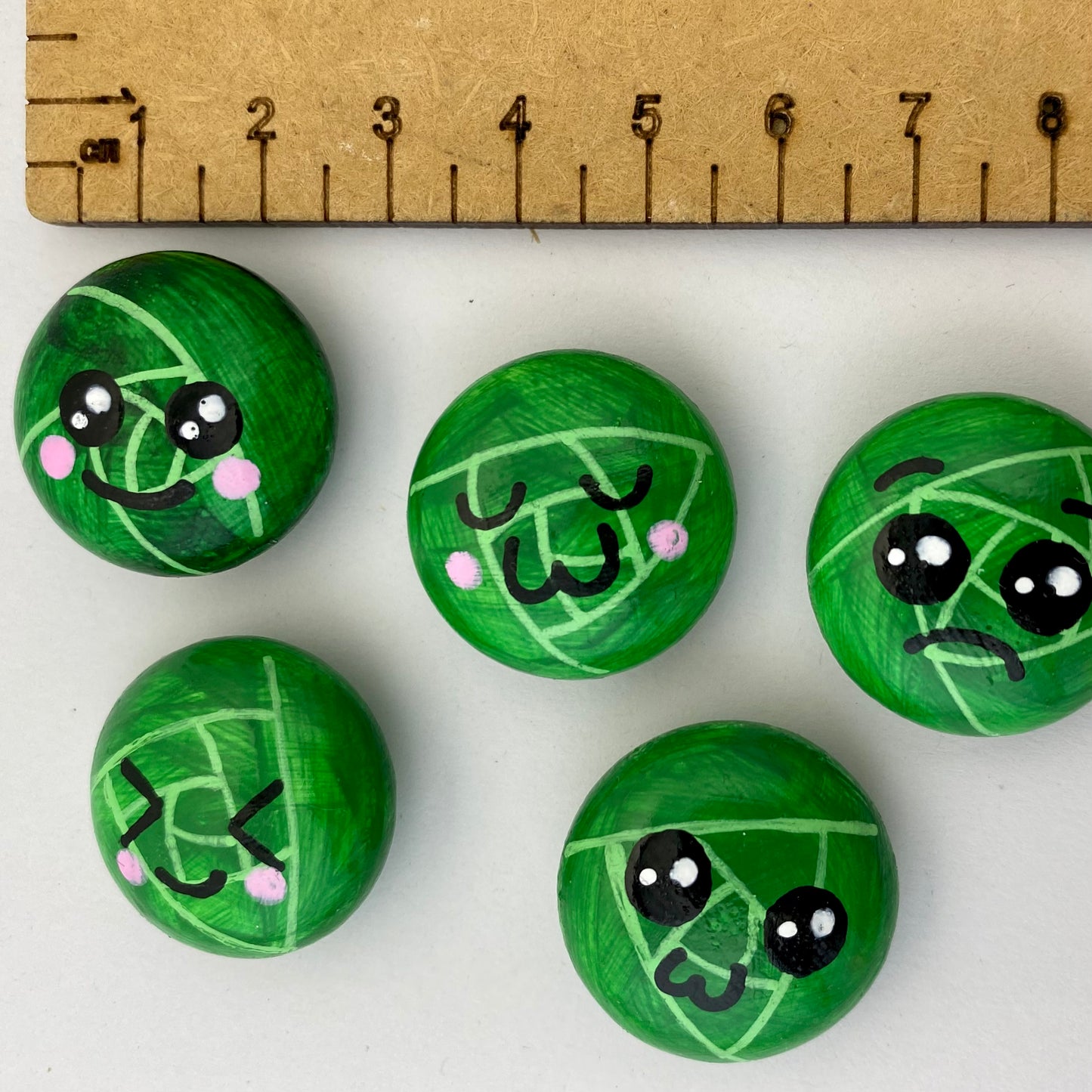 5 Hand painted tiny sprout pebbles each with a different cute faced expression next to a ruler