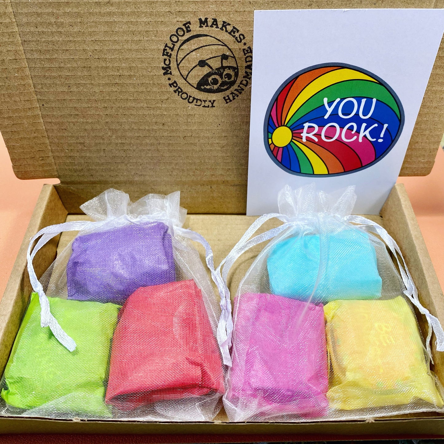 2 sets of 3 pebbles wrapped in colourful tissue paper inside organza bags with a You Rock business card and McFloof Makes stamped postal box