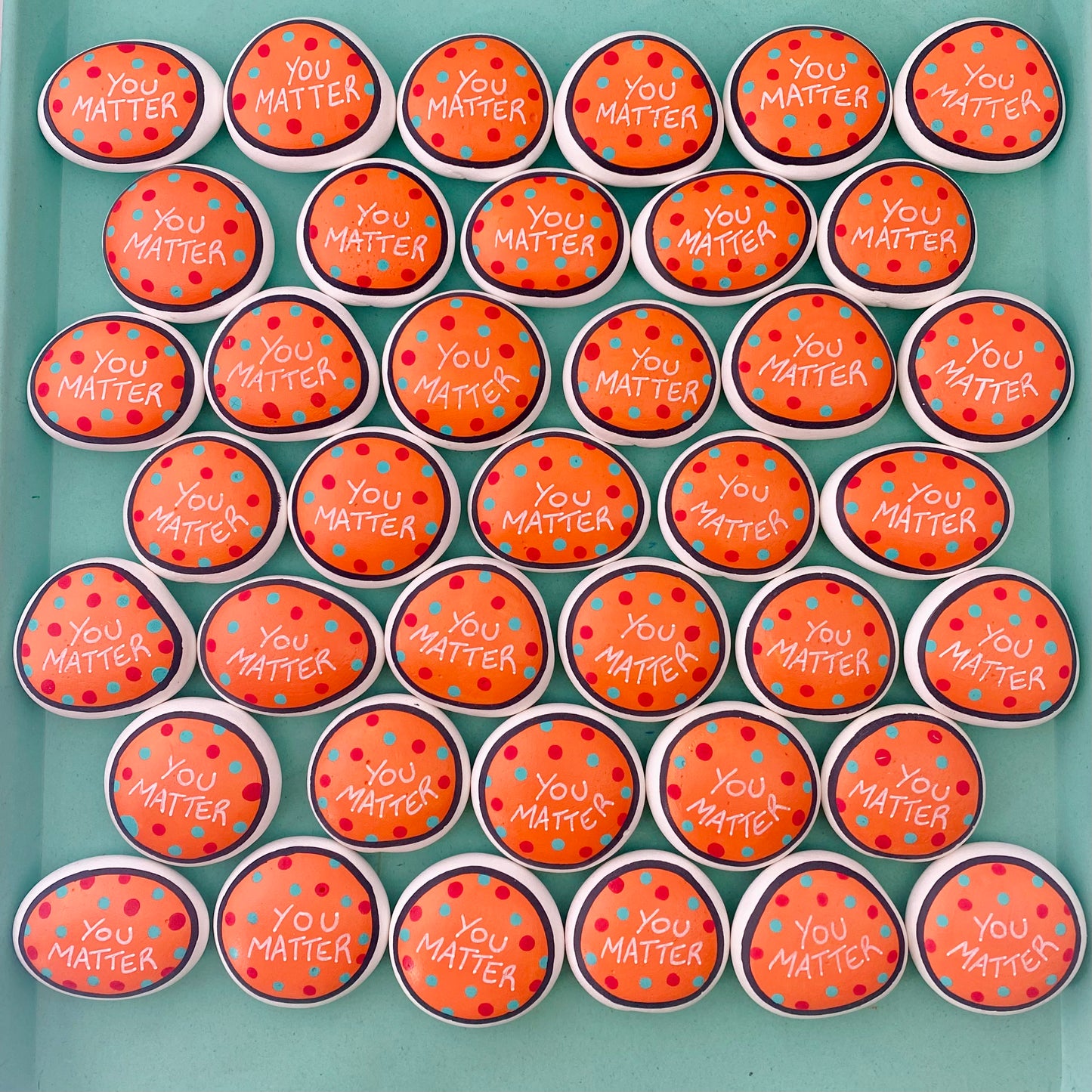 Lots of Orange Hand painted pebbles with the words You Matter written on