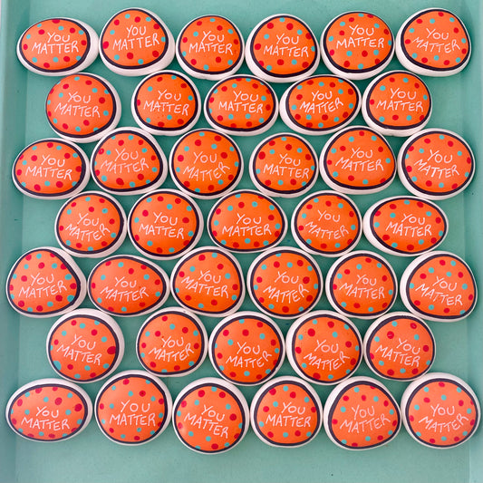 Lots of Orange Hand painted pebbles with the words You Matter written on