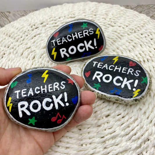 3 stones painted black with rock and roll symbols painted in bright colours and the words "Teachers Rock!" in white