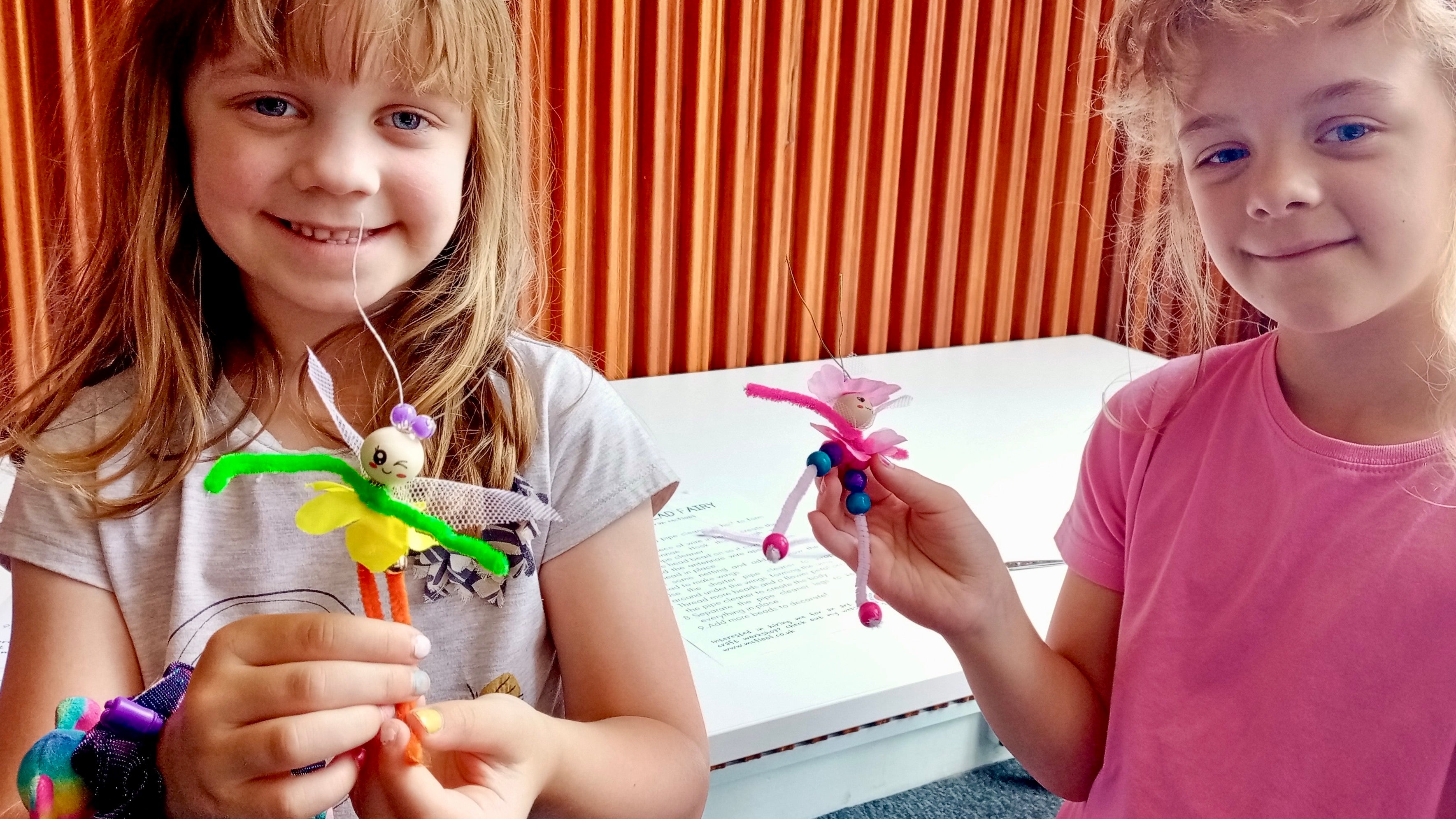 Two girls holding fairies they made from colourful pipe cleaners and beads