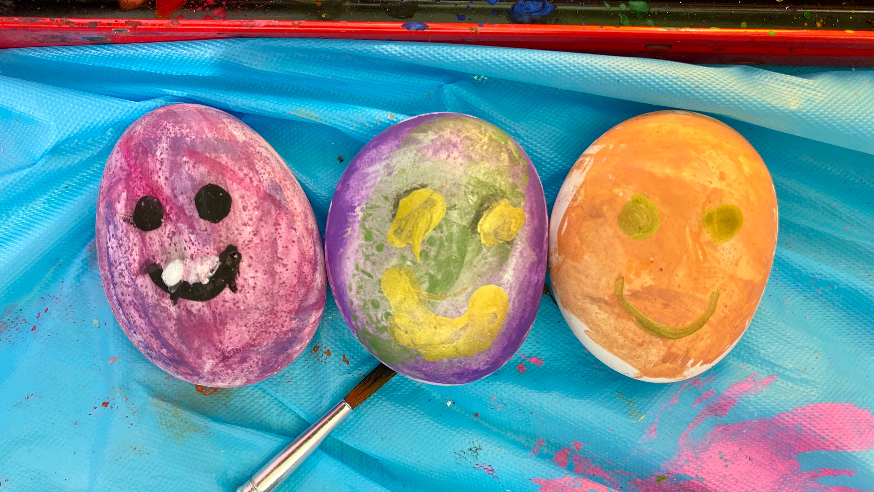 3 painted pebbles in a row with smiley faces painted on. Each a different colour.