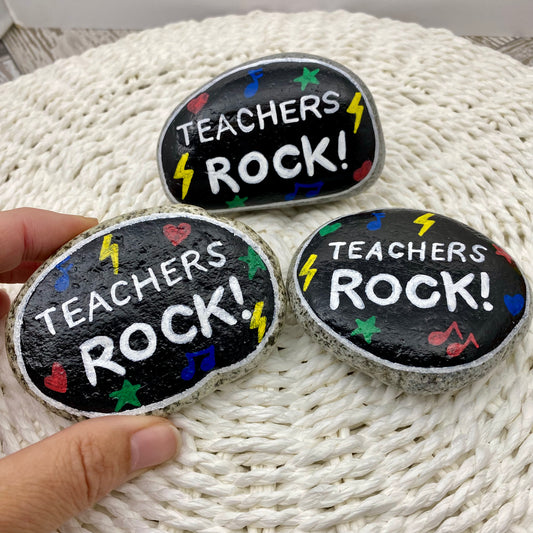 3 stones painted black with rock and roll symbols painted in bright colours and the words "Teachers Rock!" in white
