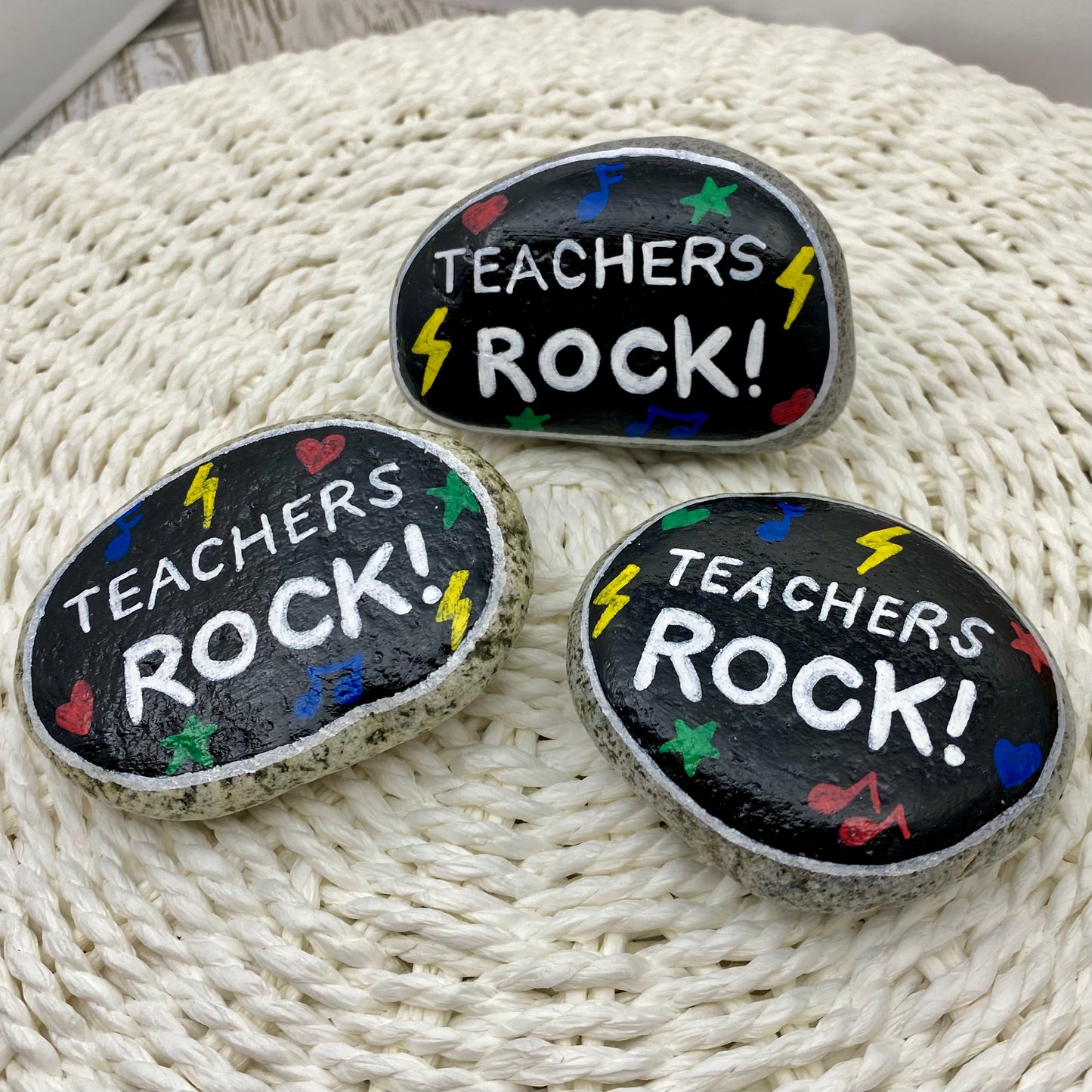 3 stones painted black with rock and roll symbols painted in bright colours and the words "Teachers Rock!" in white
