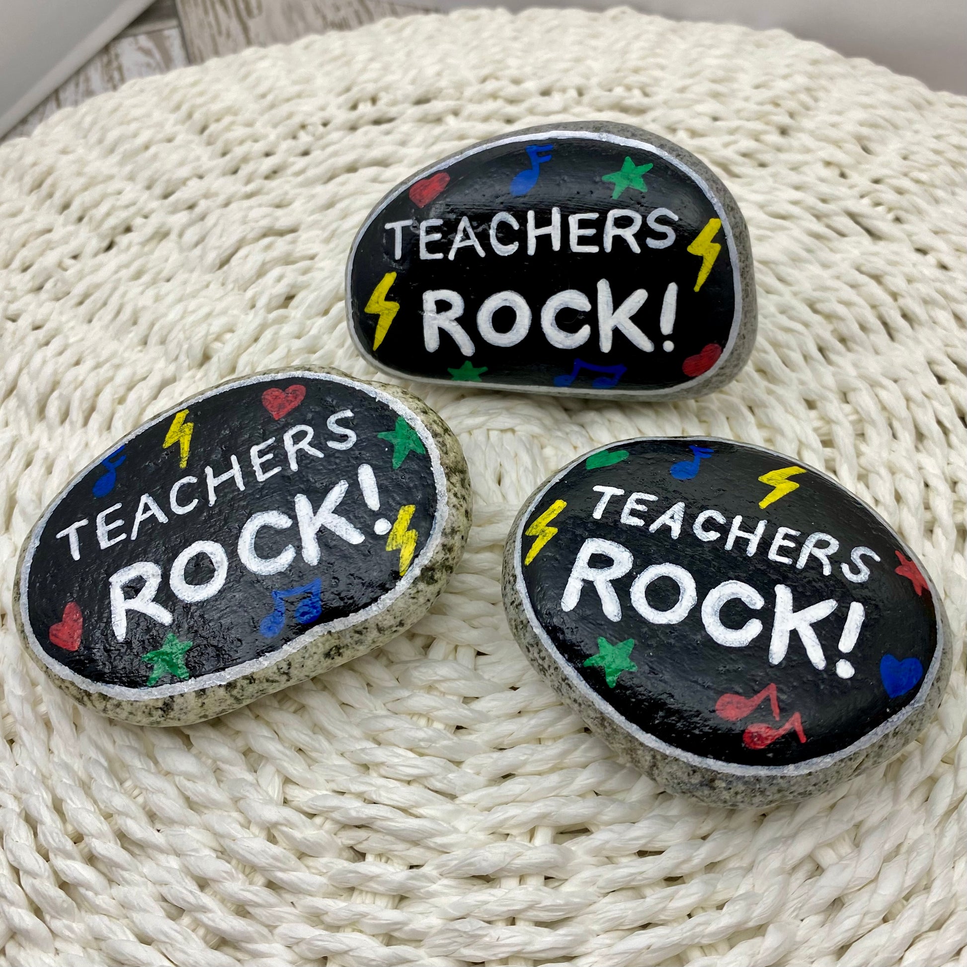 3 stones painted black with rock and roll symbols painted in bright colours and the words "Teachers Rock!" in white