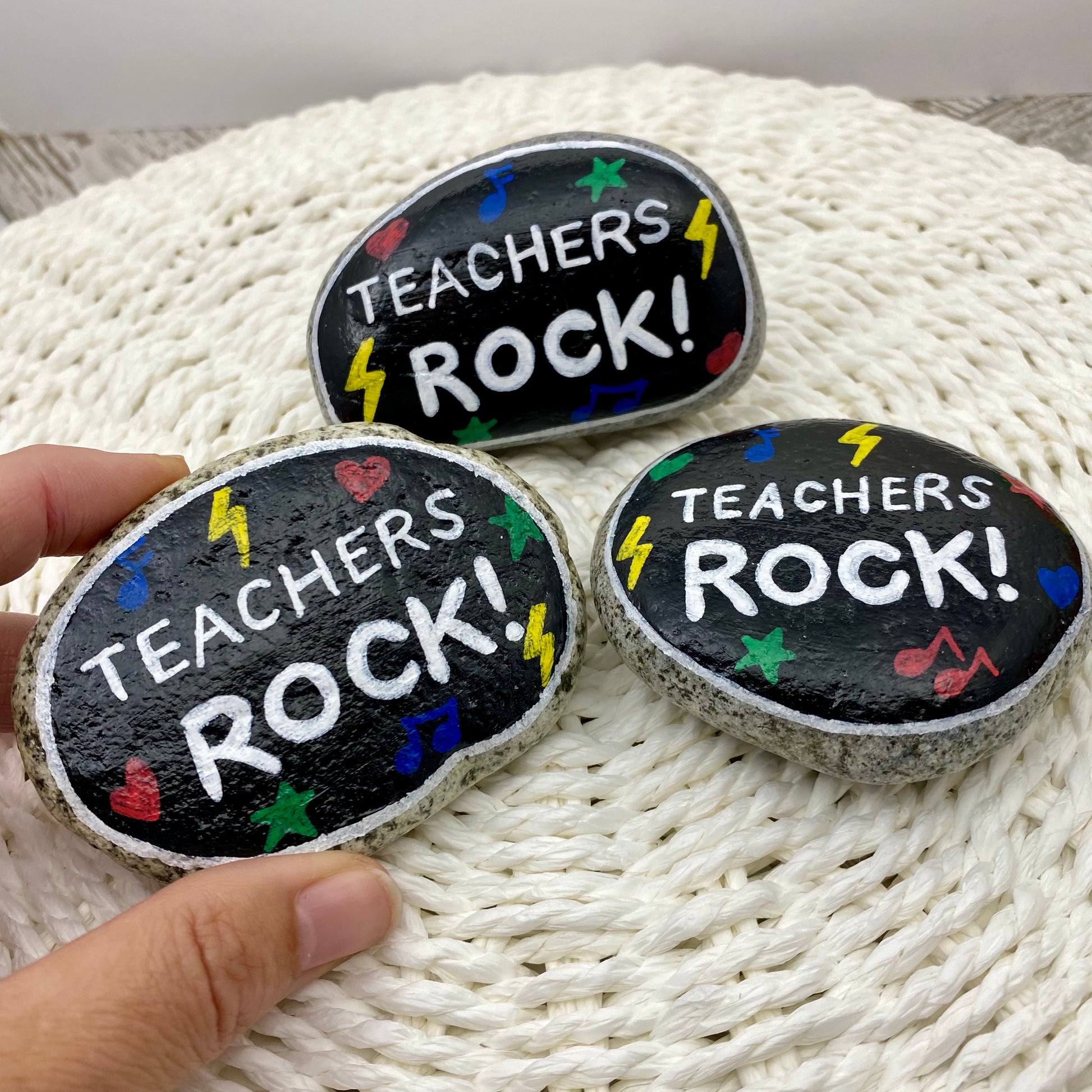3 stones painted black with rock and roll symbols painted in bright colours and the words "Teachers Rock!" in white
