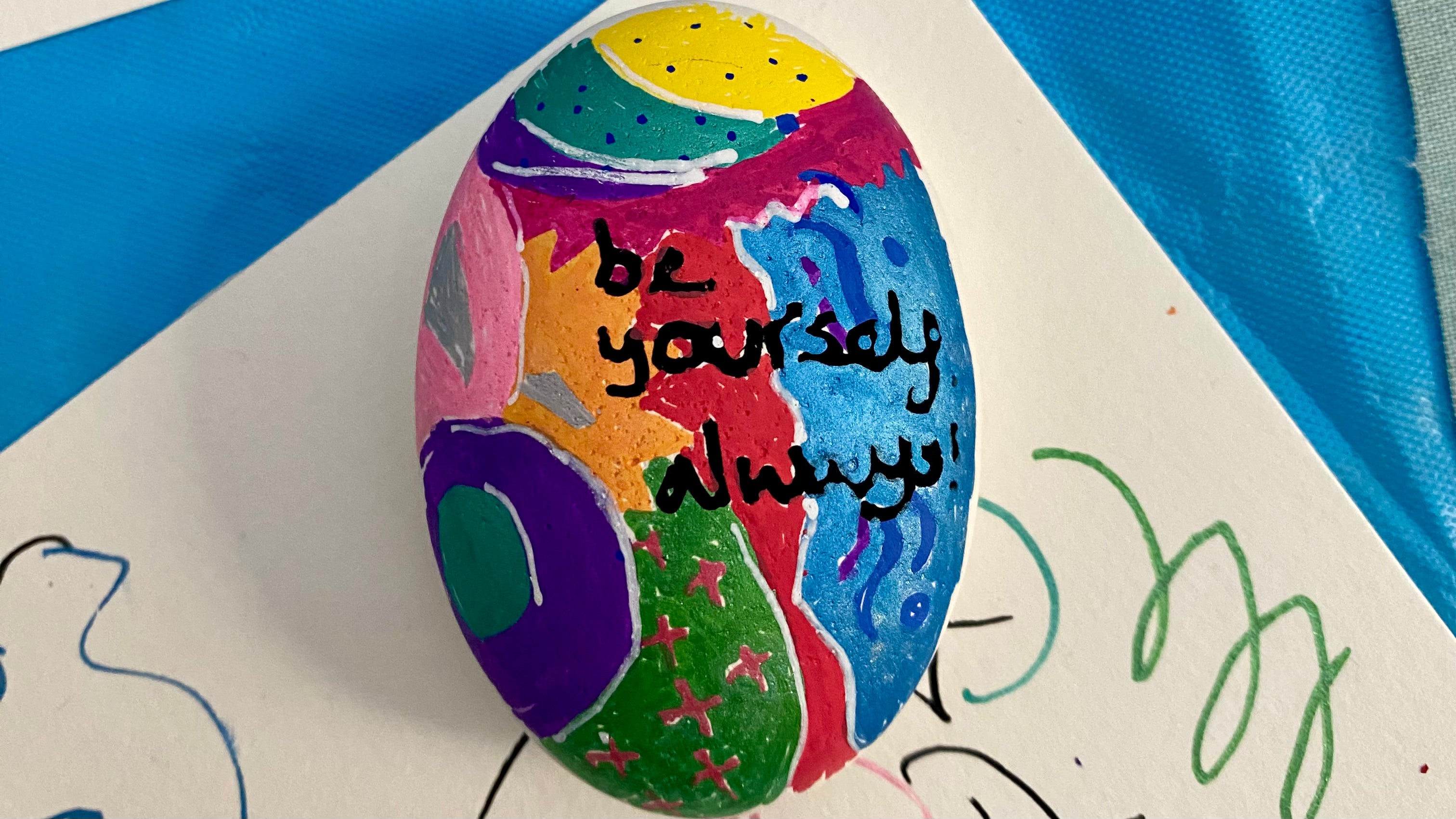 A brightly coloured and patterned painted pebble with the words Be Yourself Always written on