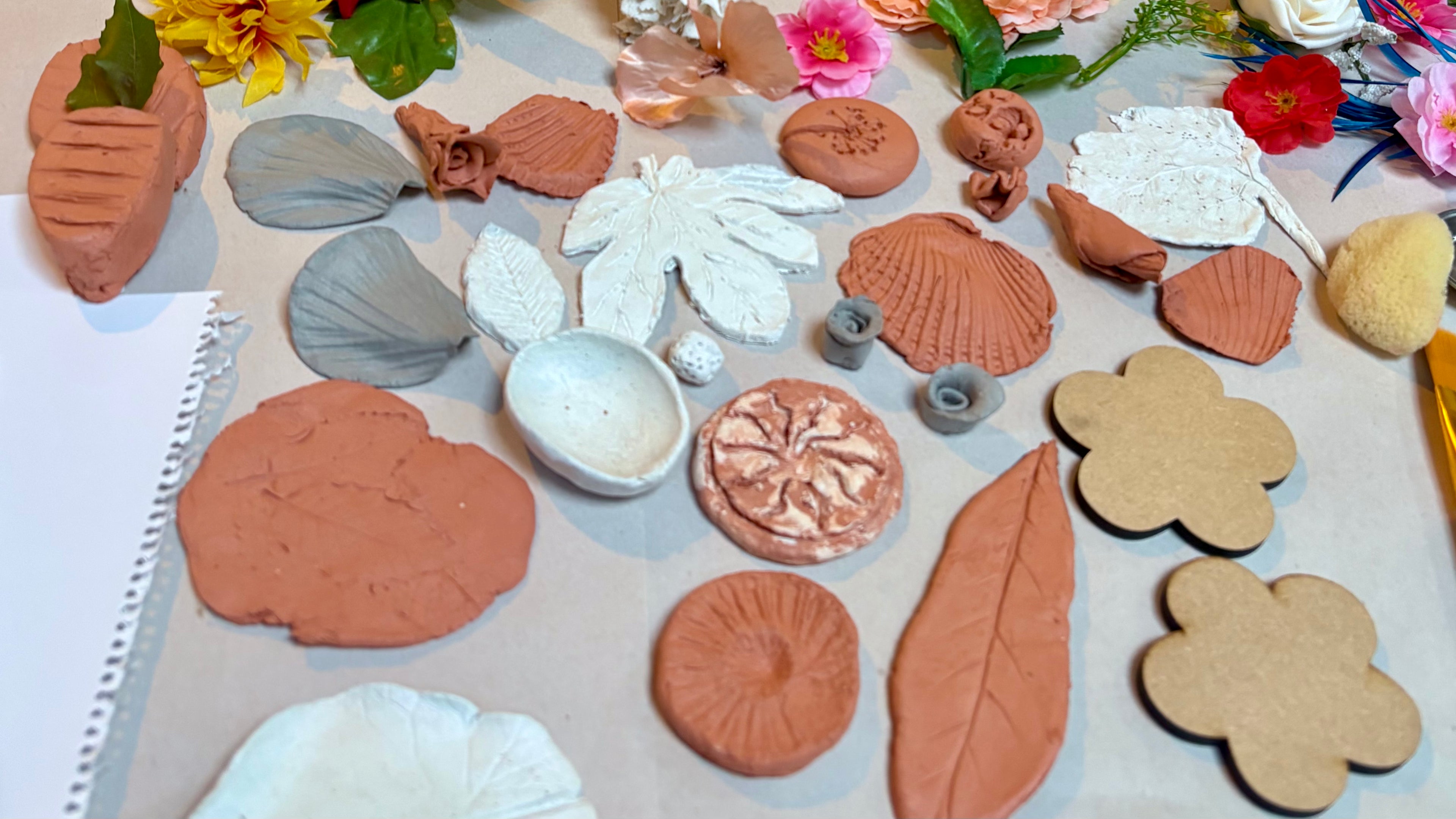 A table full of small clay leaf and flower creations, with leaves and flowers around