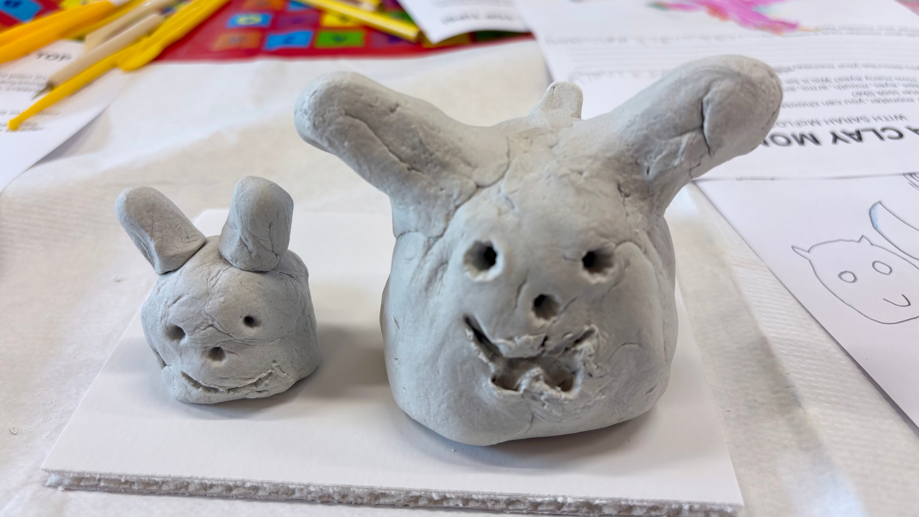 Two clay monster rabbit sculptures on a table with art supplies in the background