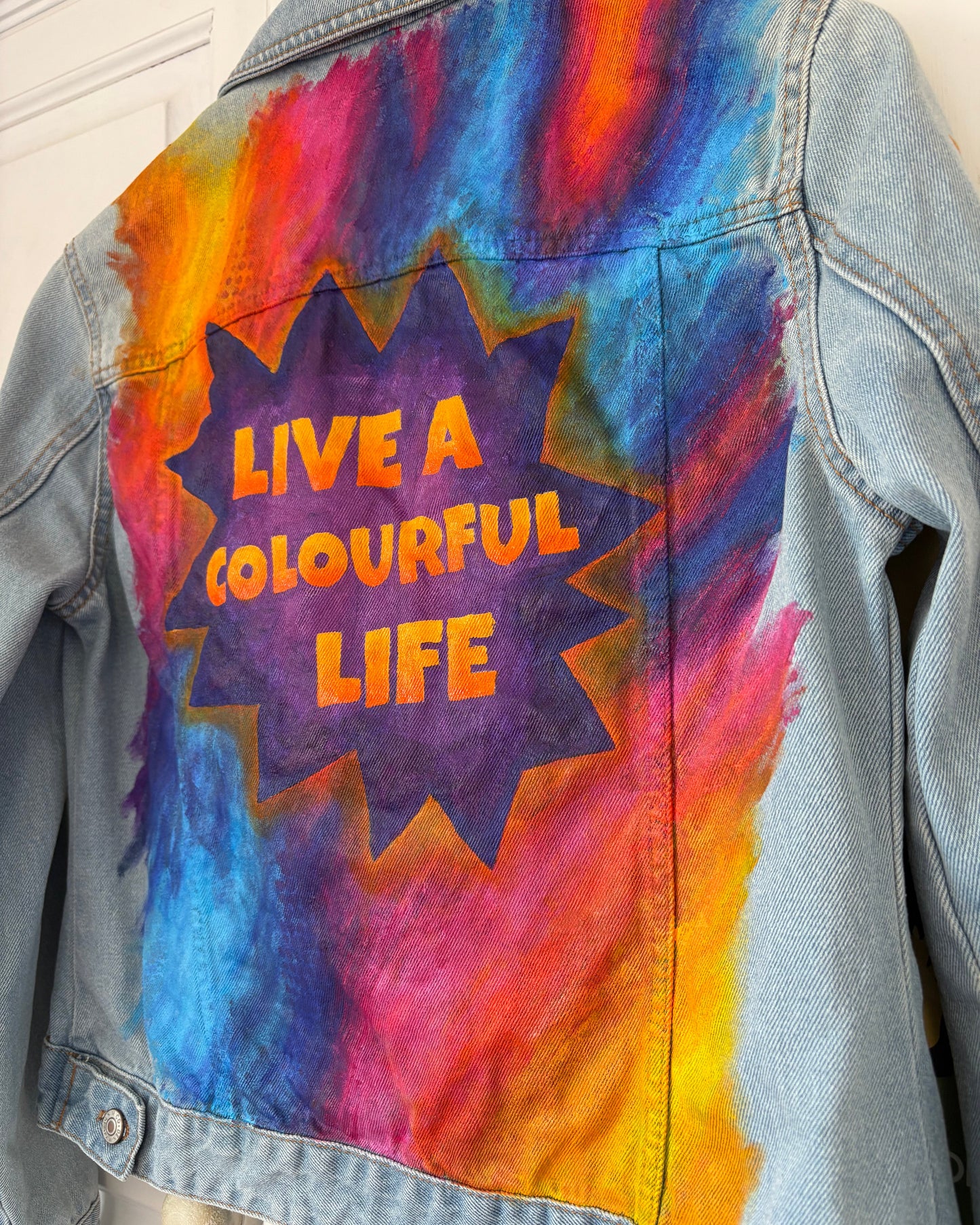 Denim jacket with colourful grafitti style design and 'Live a Colourful Life' text painted in a purple starburst.