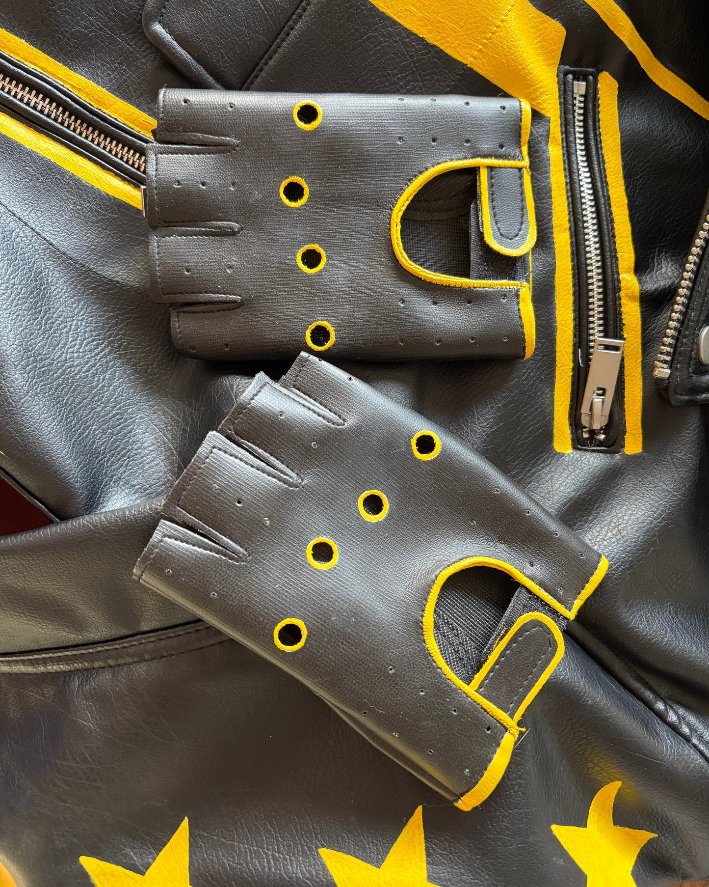 Black leather gloves with yellow accents on a black leather jacket with yellow star patterns.