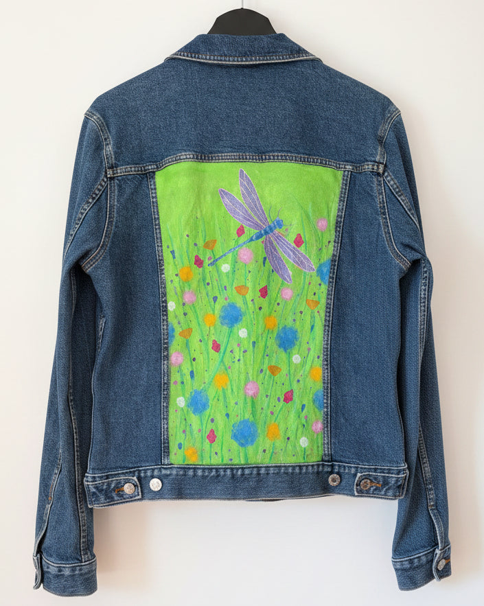 Blue denim jacket with a painted green wildflower meadow featuring a shimmering dragonfly design