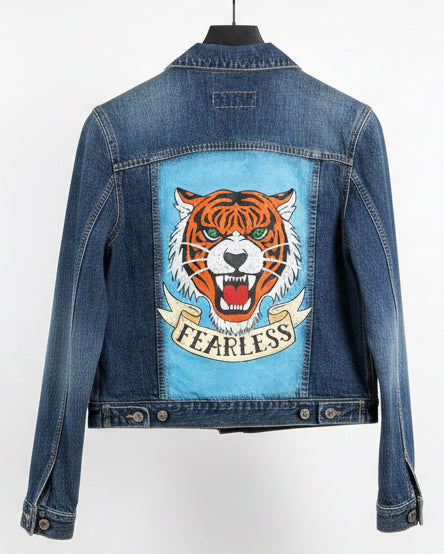 Back of a handprinted denim jacket with a flash style tiger face with it's mouth open and the word Fearless written underneath on a banner