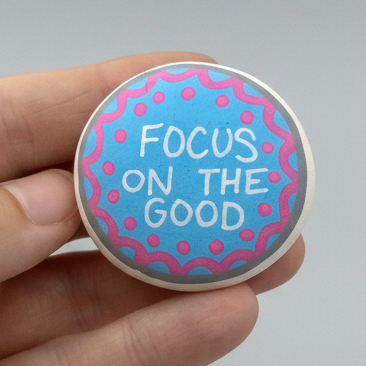 Hand holding a Colourful blue Hand painted white pebble with the words Keep Growing written on in white. Pink dots and wiggle lines painted around the edge of the pebble.