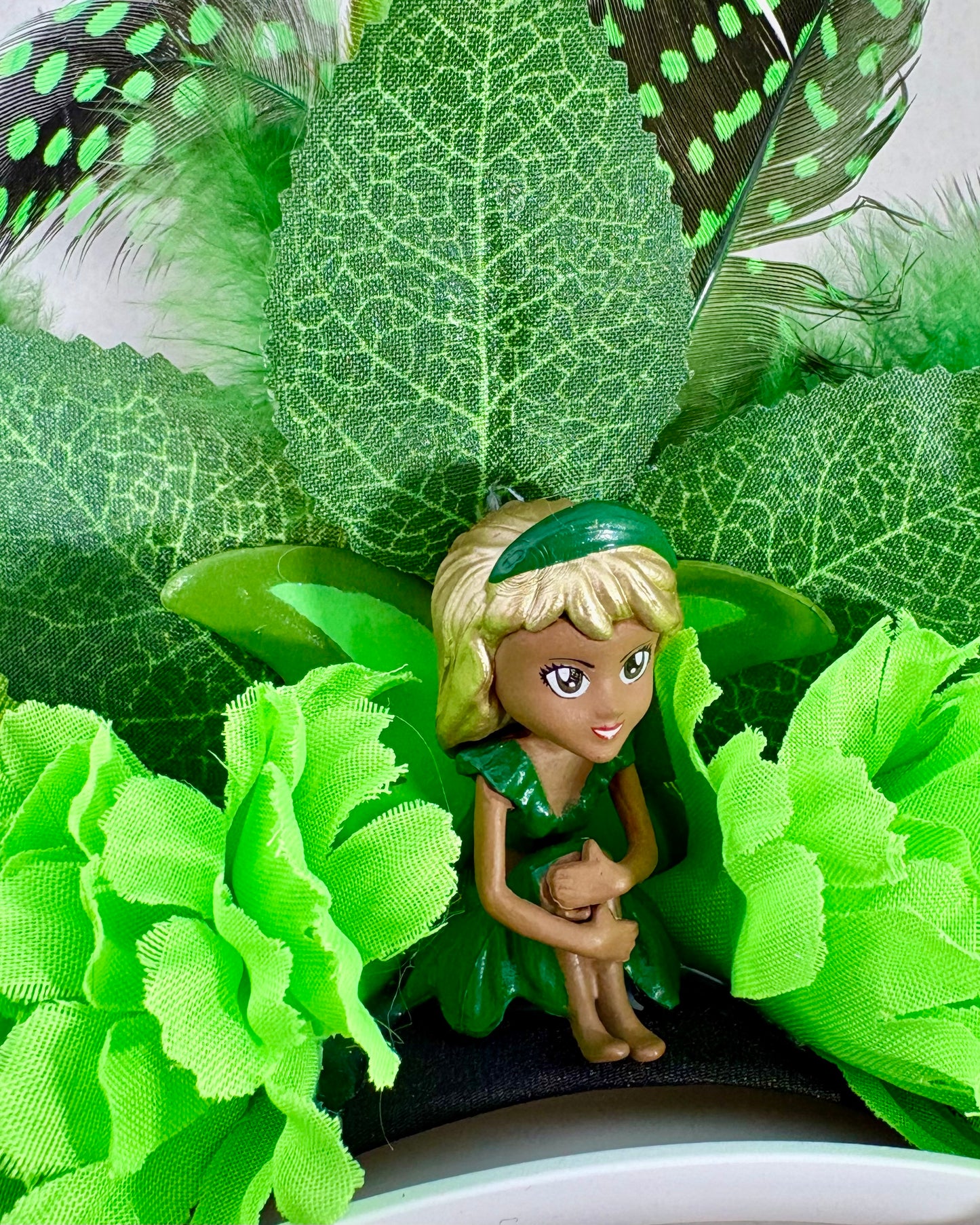 Toy fairy figure surrounded by green leaves, flowers and feathers on a festival crown