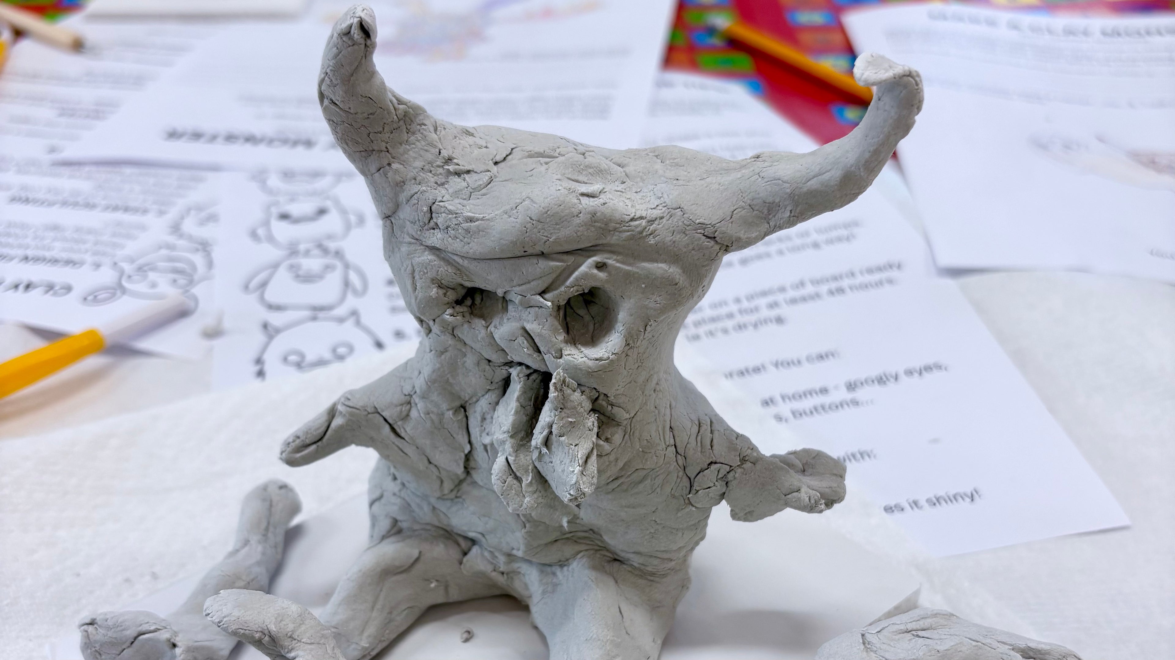 Clay sculpture of a horned creature on top of papers with clay tools