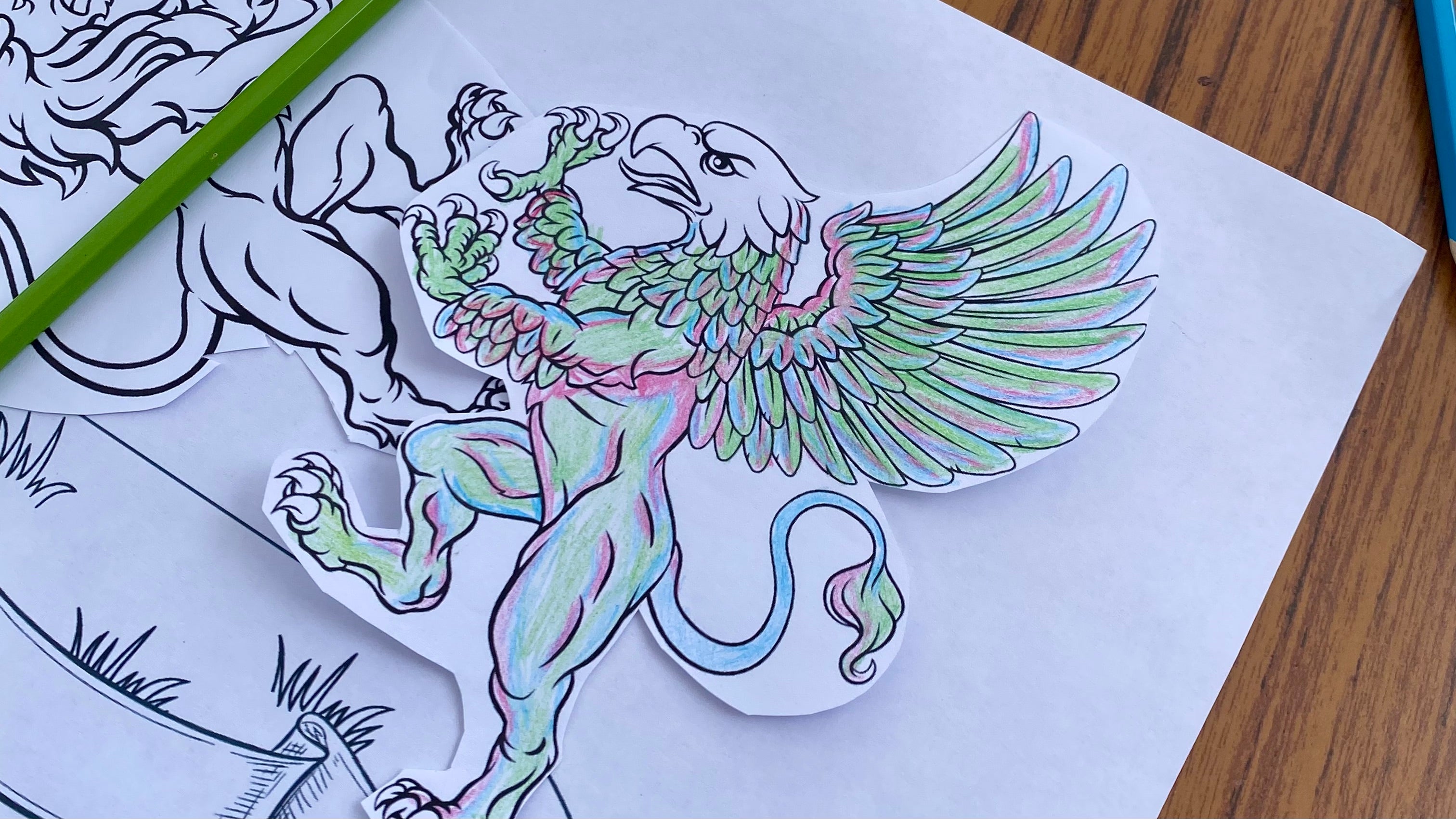 A section of a crest in the process of being coloured in with colouring pencils. A griffin with the colours glue, green and pink.