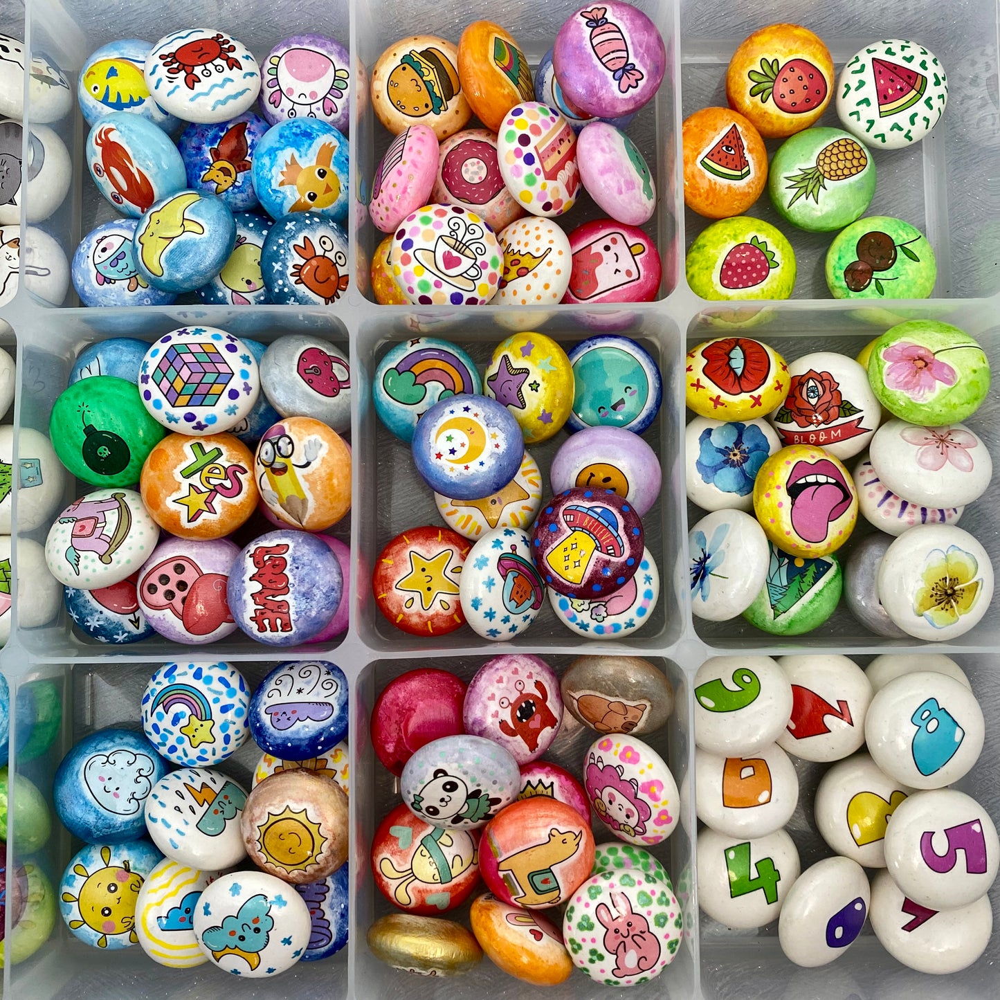 Lots of colourful mini pebbles in a tray, sorted by theme. Ocean, Sweets, Fruit, Fast Food, Weather, Flowers, Galaxy, Creatures, Numbers and Nostalgic Toys.