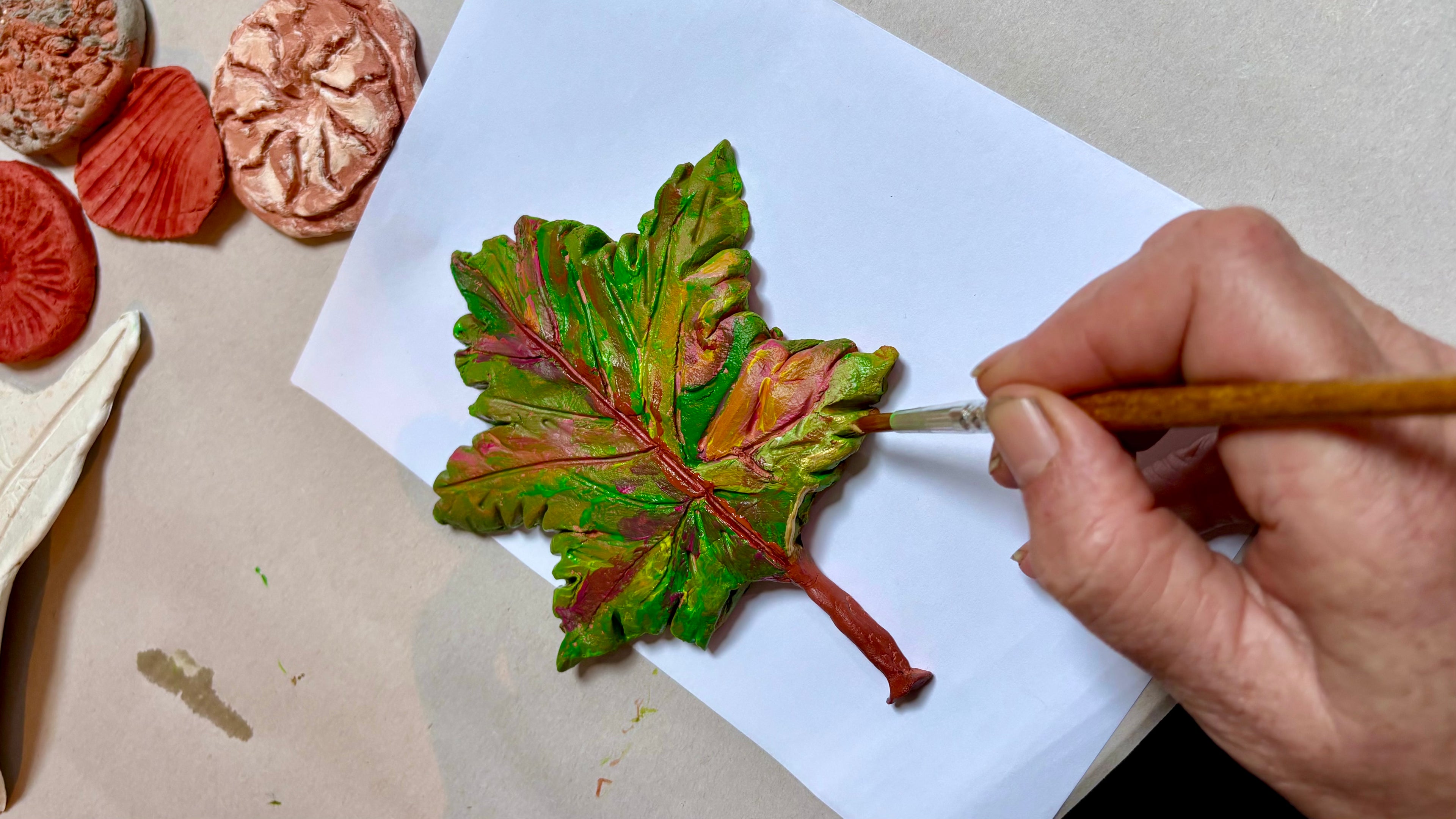 Clay oak leaf being painted with greens, reds, oranges, browns and gold