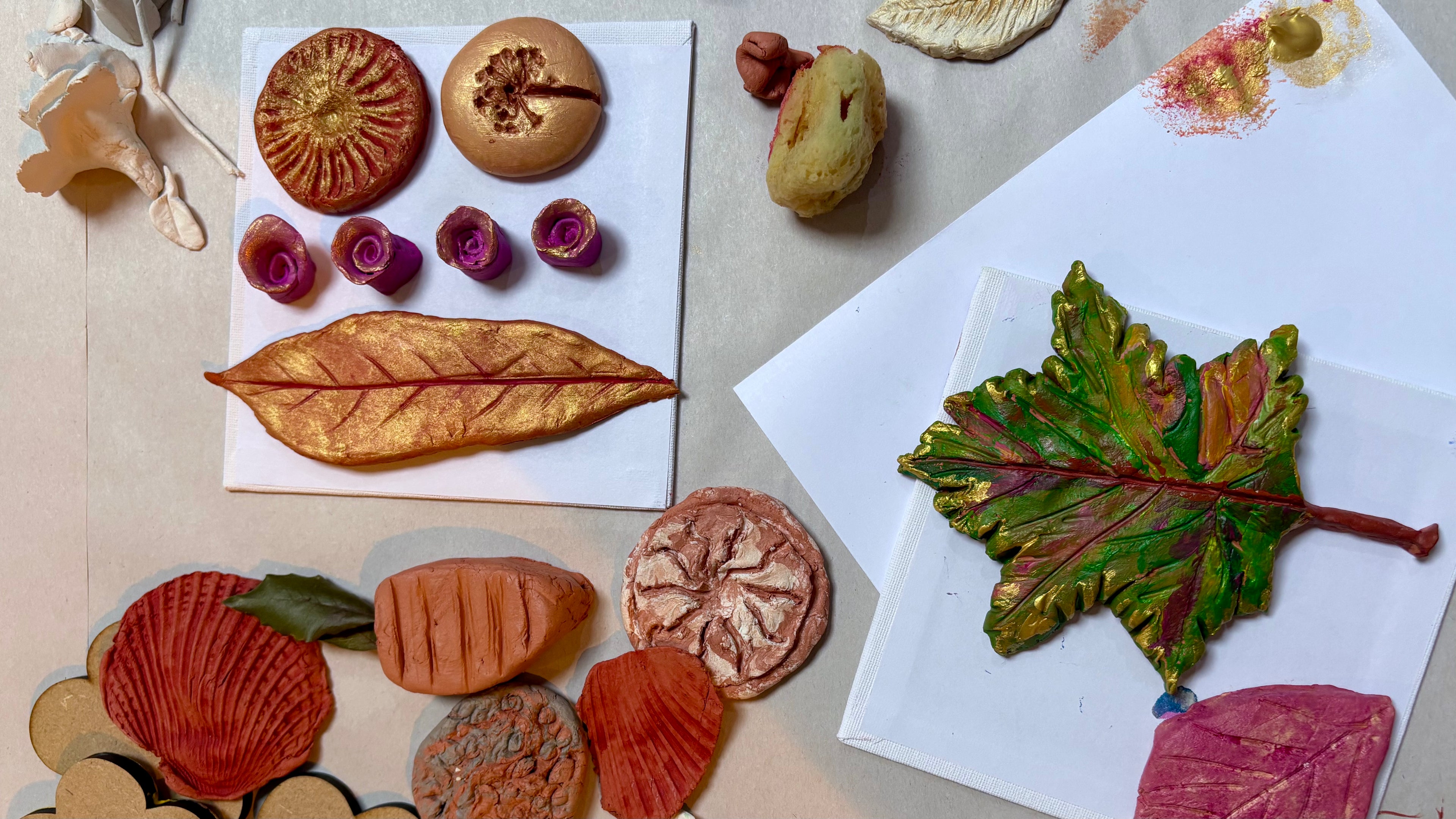 An overhead flat-lay of colorful painted clay flower and leaf shapes arranged on white paper