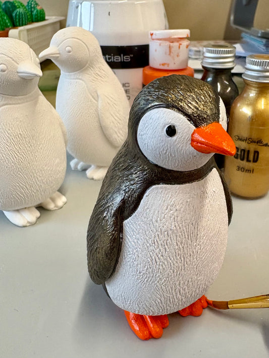 Painted penguin statue with penguin blanks and paints in the background