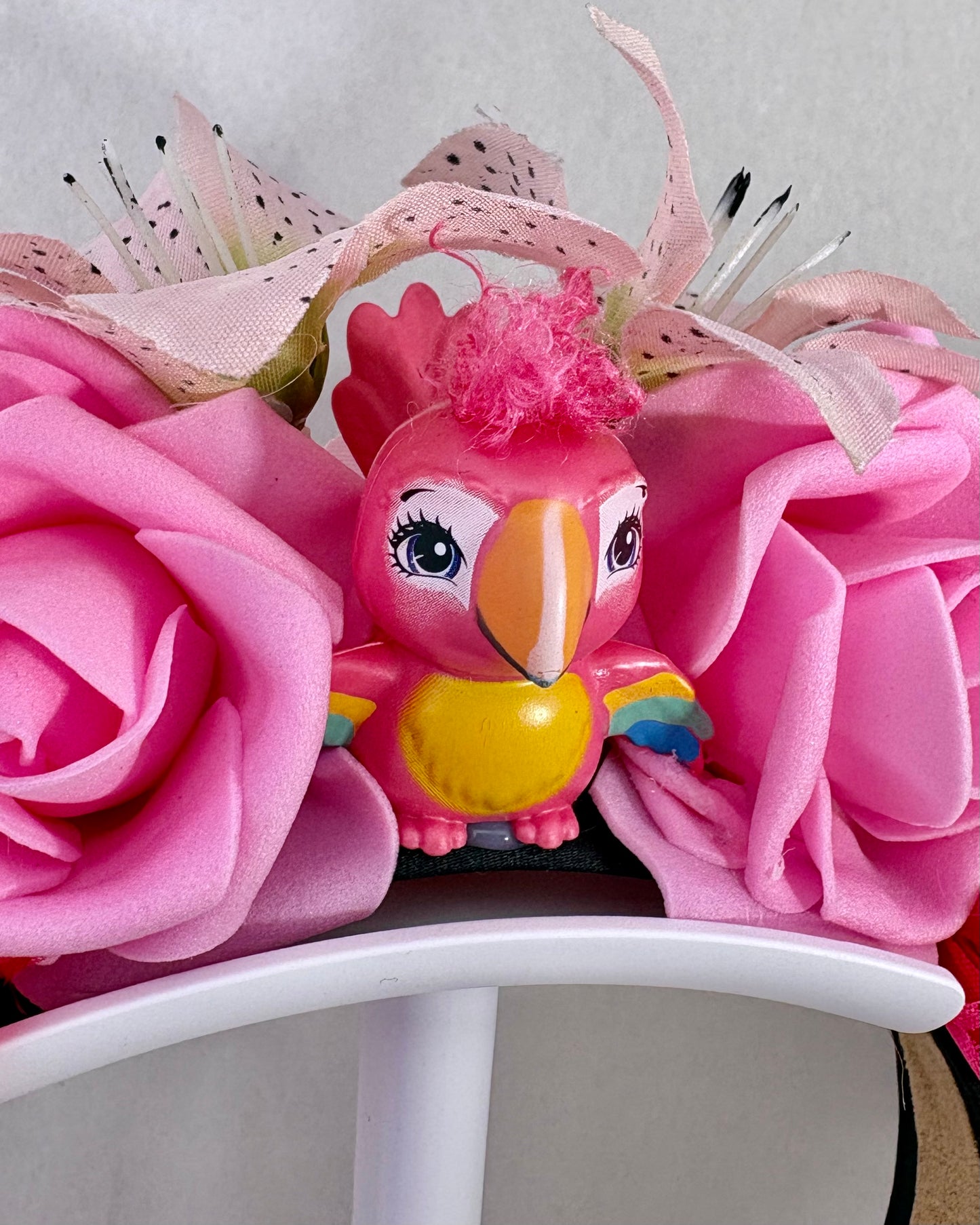 Close up of Headband with pink flowers and a small toy parrot figurine