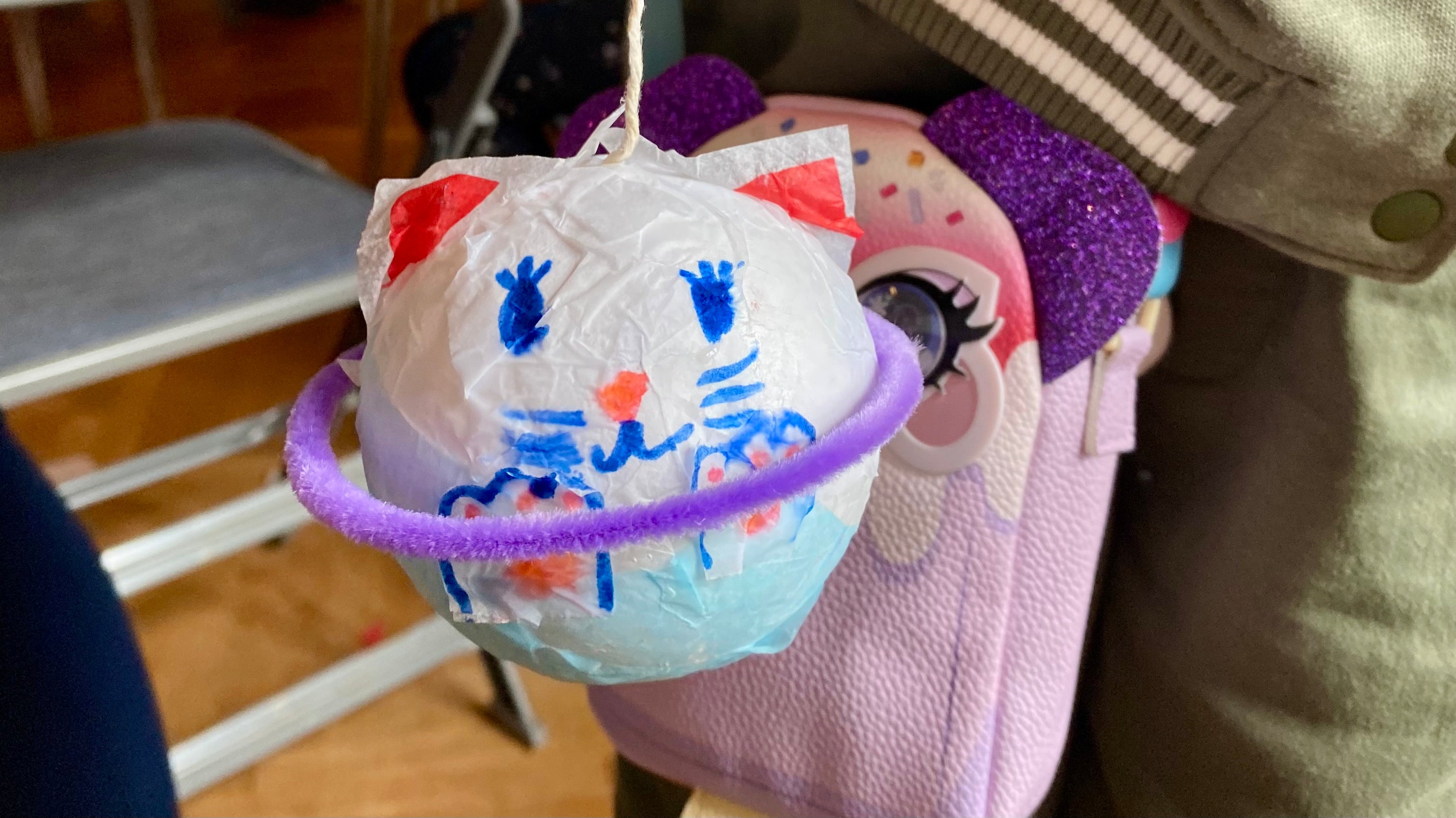 A handmade paper mache planet in the shape of a cat with a pipe cleaner ring around the middle being held up with string