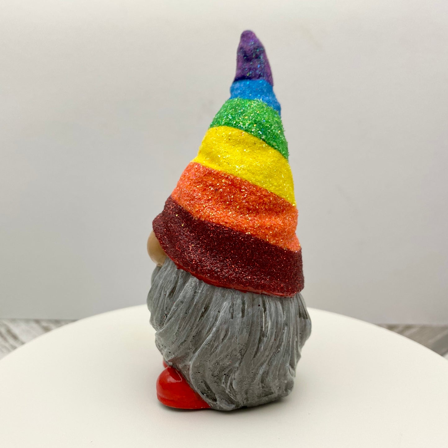 Small hand painted gonk statue with a Glittery Rainbow hat, grey beard and red shoes. Side view.