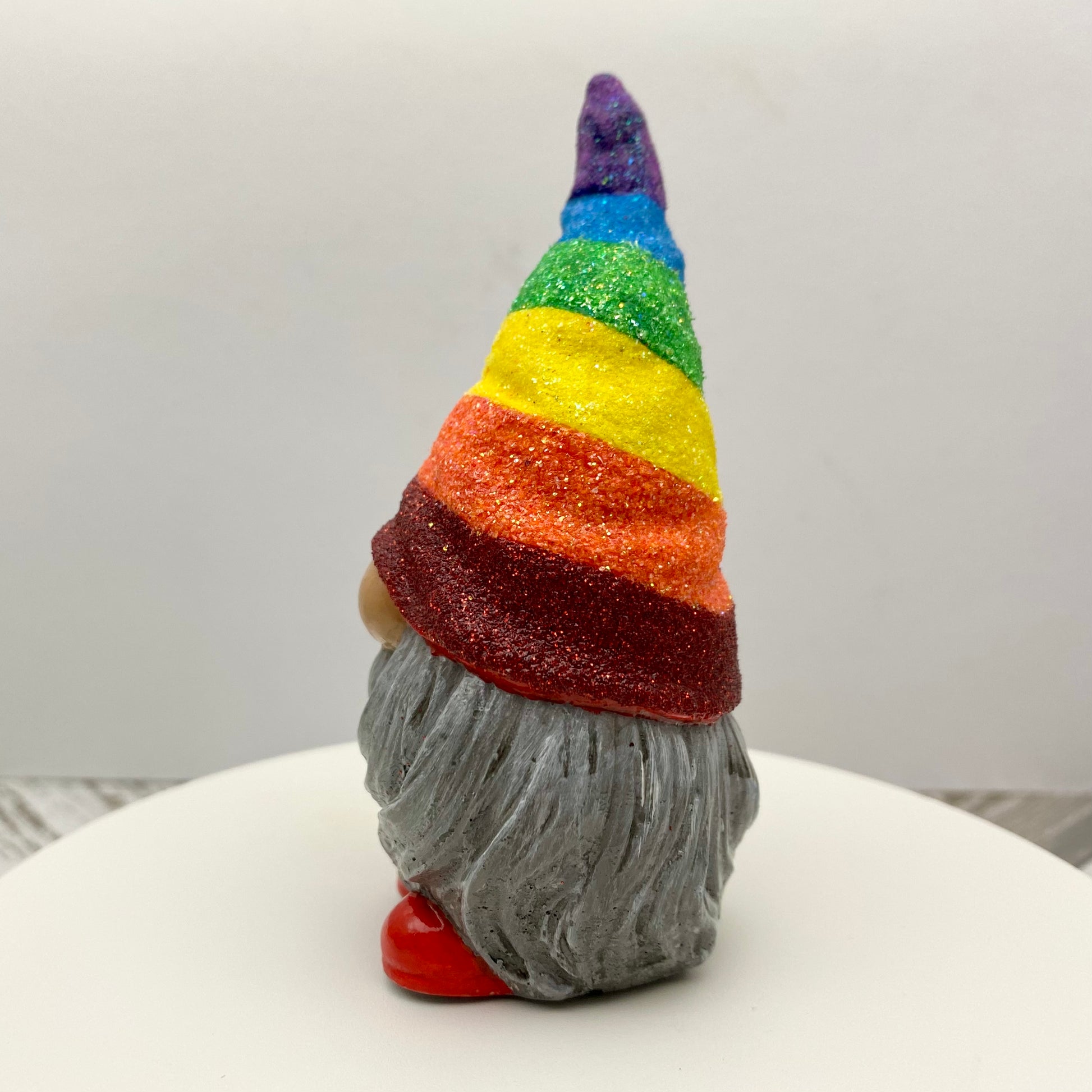 Small hand painted gonk statue with a Glittery Rainbow hat, grey beard and red shoes. Side view.