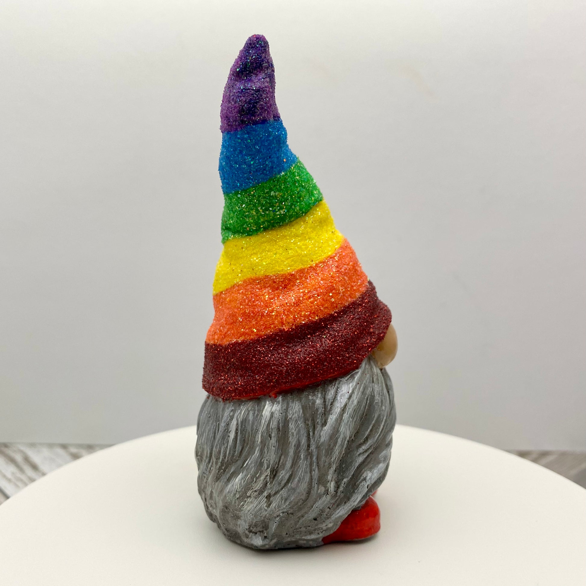 Small hand painted gonk statue with a Glittery Rainbow hat, grey beard and red shoes. Side view.