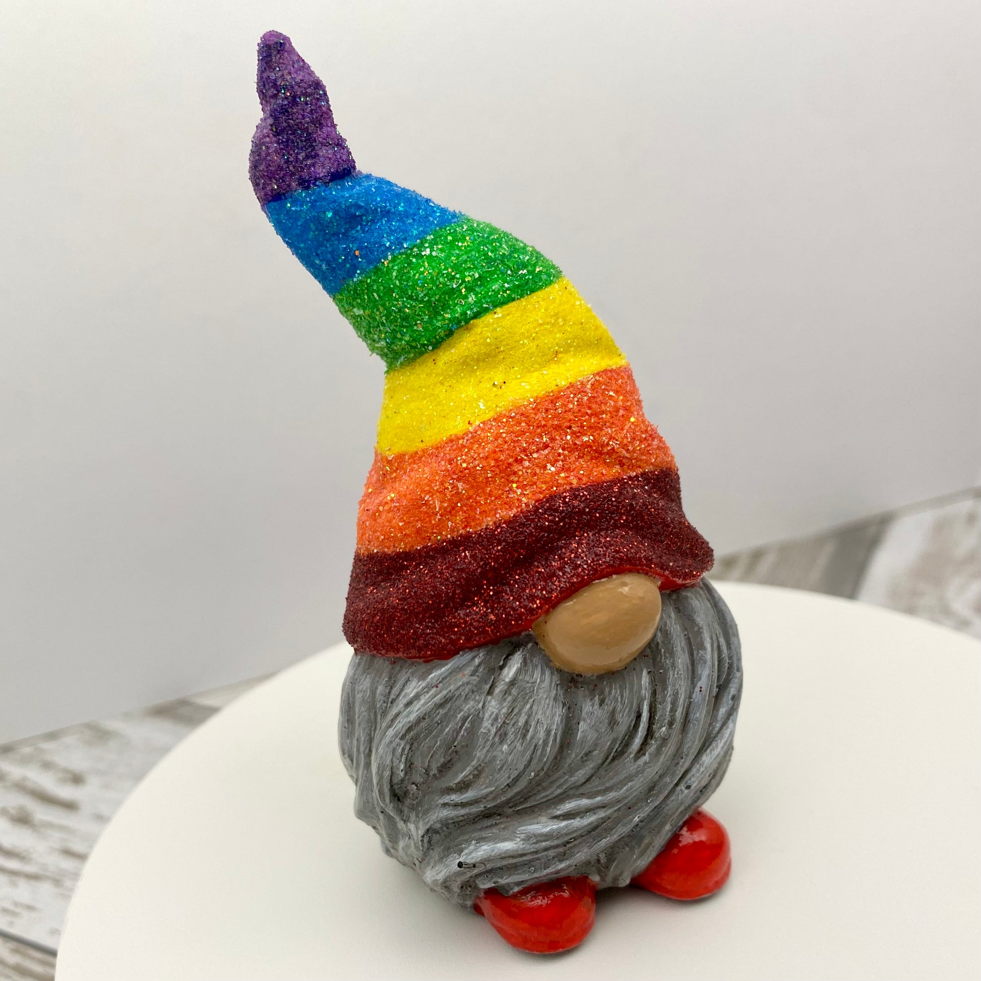 Small hand painted gonk statue with a Glittery Rainbow hat, grey beard and red shoes. Side view.