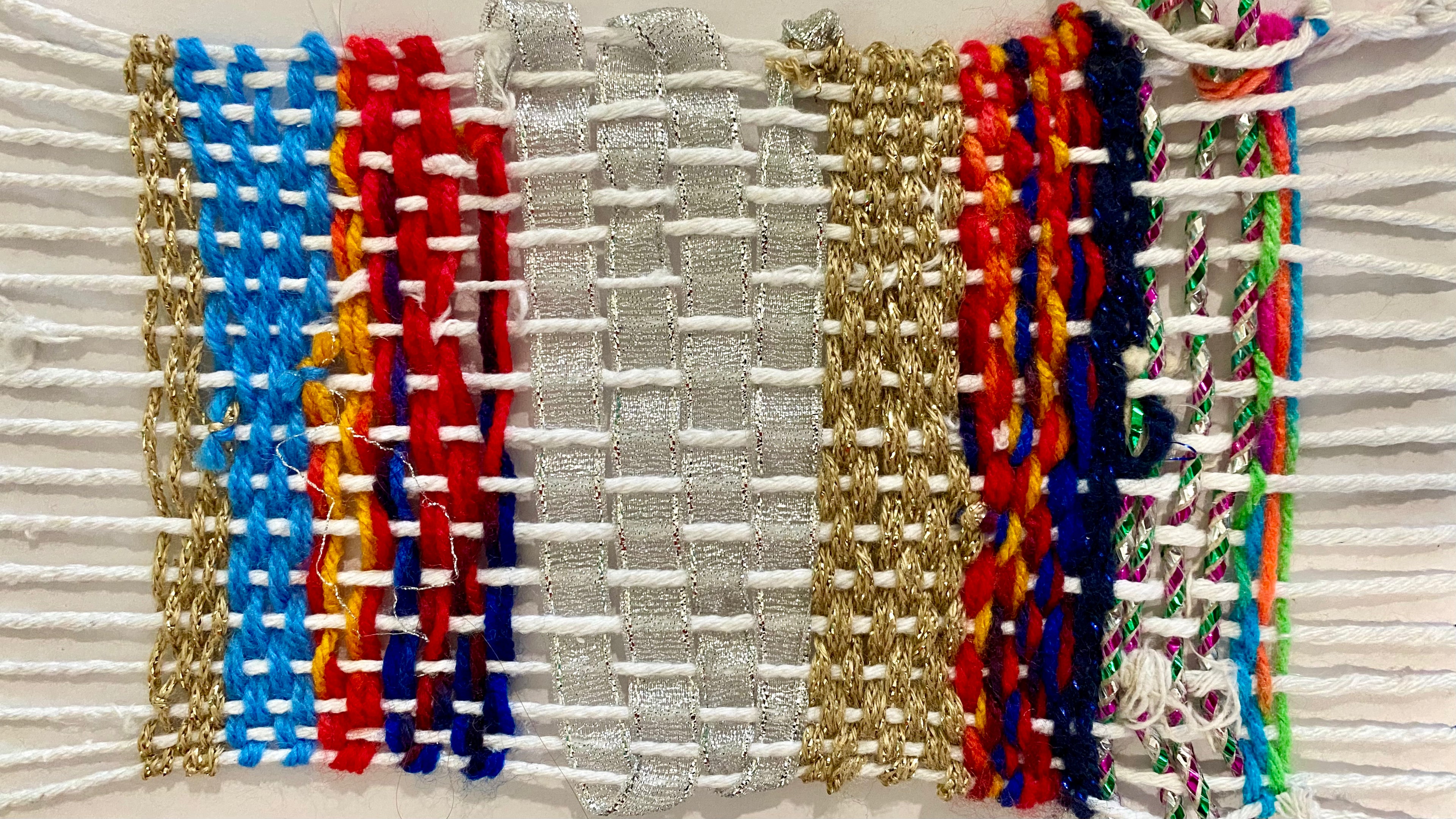 A card weaving loom with strings and colourful scraps of fabric, wool and ribbons weaved onto it.