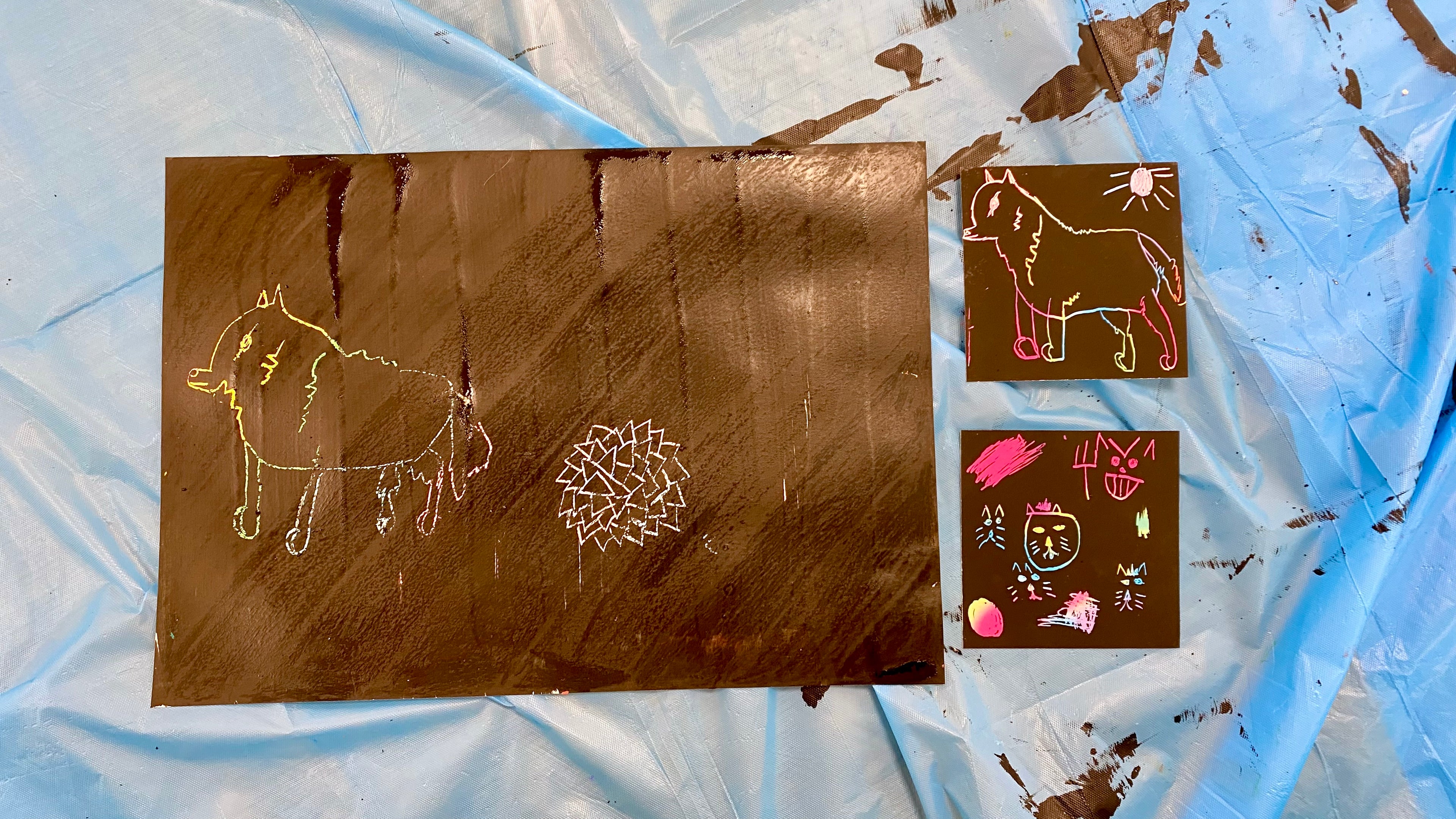 2 pieces of scratch art paper with designs etched in. One has a wolf and a succulent, one has a dog and sunshine, one has several cat faces. Colours from the layer beneath showing through.