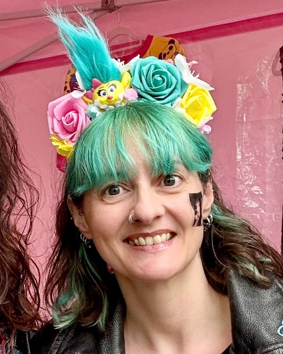 A woman with green and brown hair wearing a troll themed hair crown with greens, pink and yellow roses.