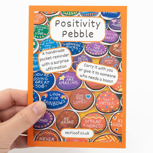 Packaging of Positivity Pebble with colourful pebbles and text on a label in an orange envelope.
