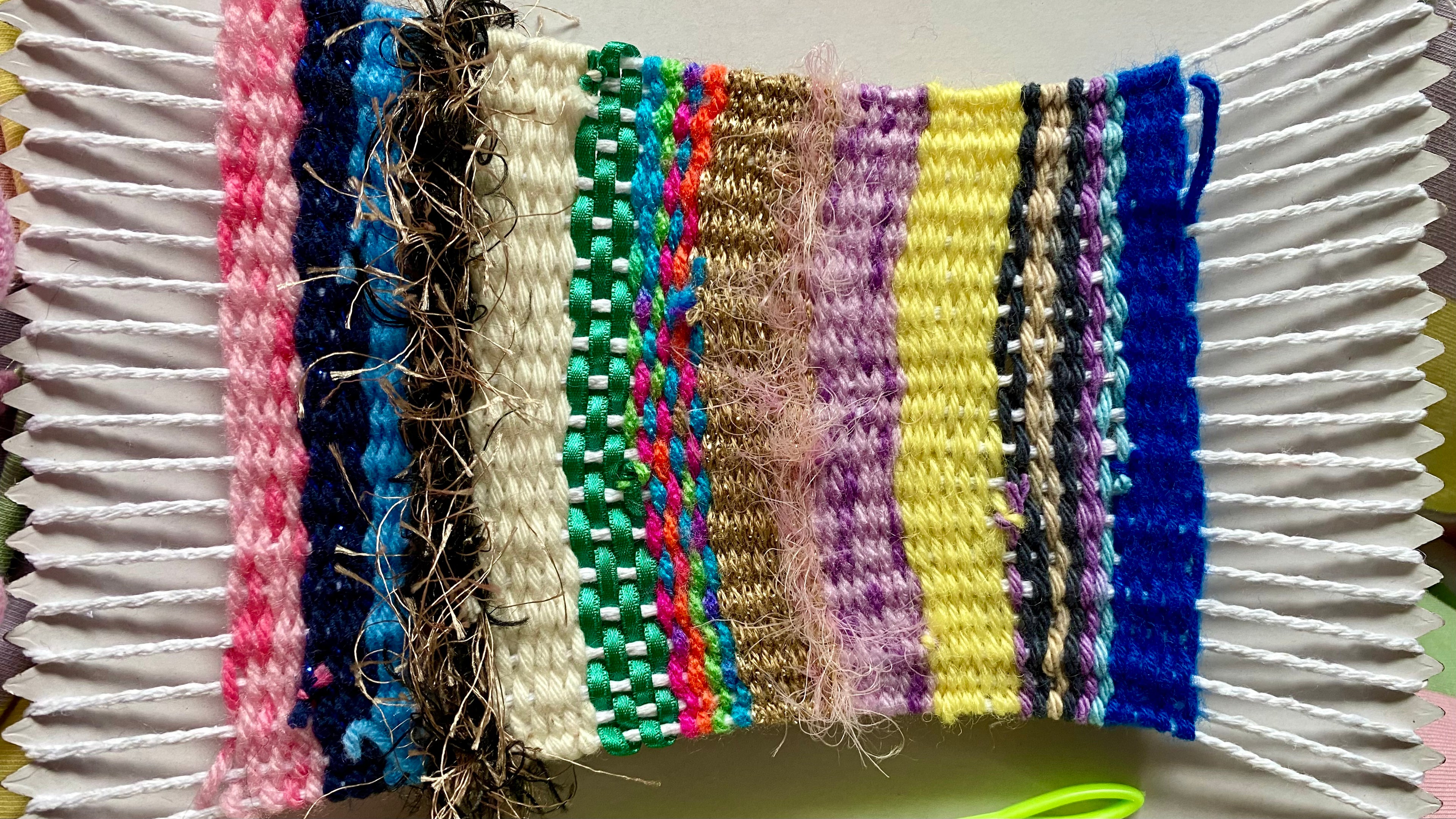 A card weaving loom with strings and colourful scraps of fabric, wool and ribbons weaved onto it.