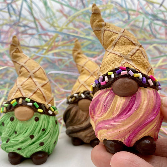3 small hand painted gonk statues painted to look like upside down ice creams. They have cream waffle hatched hats with a chocolate brown line and colourful sprinkles around the rim, one has a pink and cream striped beard, one has a mint green beard with chocolate brown dots and one has a brown striped beard. Each have chocolate brown shoes. There is colourful shredded paper in the background.