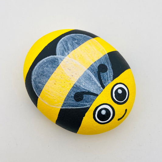 A Smooth Hand painted Yellow and Black Bee Pebble with lightly sparkling wings, and a cute face with big painted eyes.
